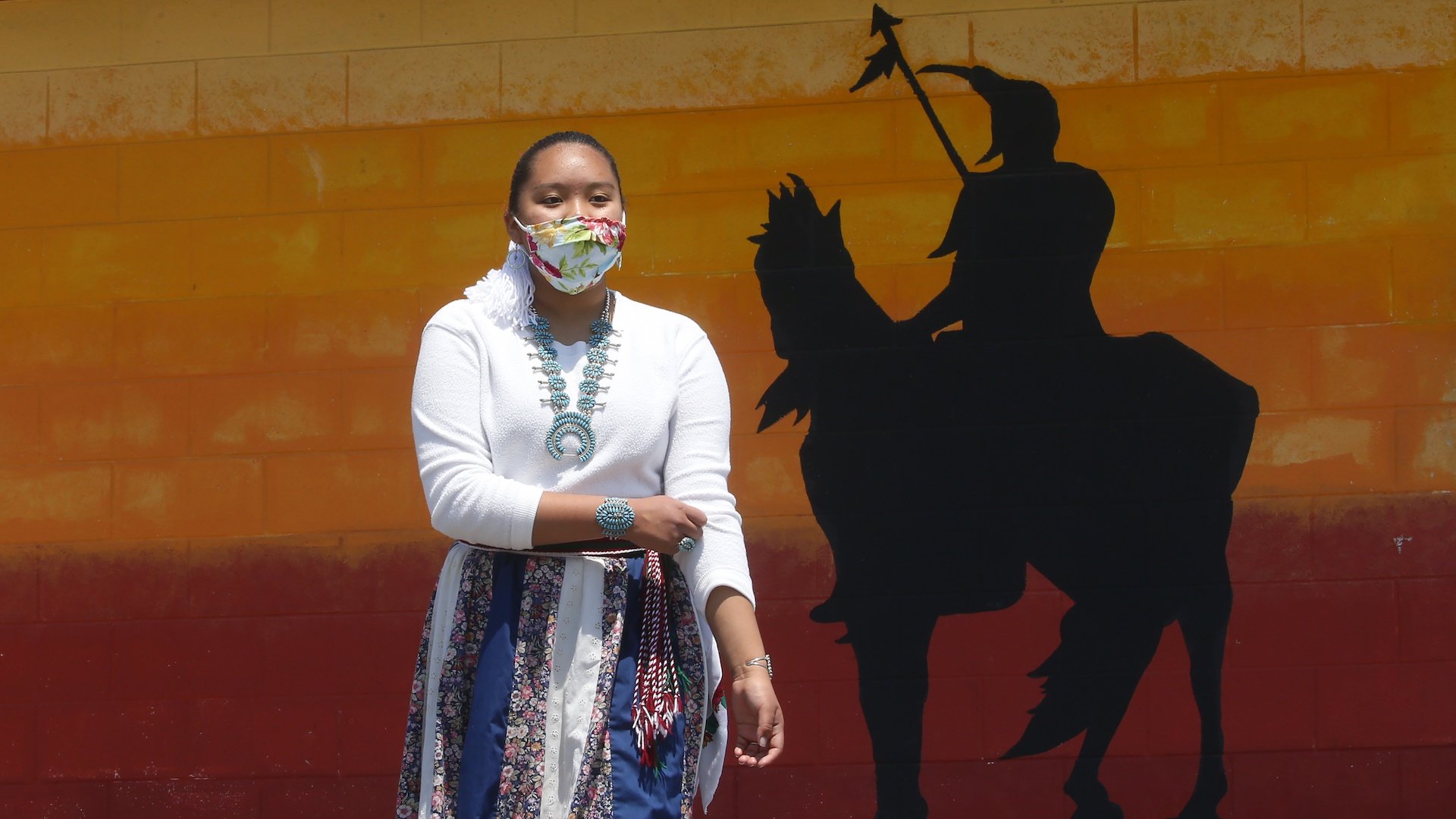 Lemiley Lane, a Bountiful junior who grew up in the Navajo Nation in Arizona, walks along the campus near a a mural of an Indigenous man meant to represent the Braves mascot at Bountiful High School, July 21, 2020, in Bountiful, Utah. (AP Photo/Rick Bowmer)