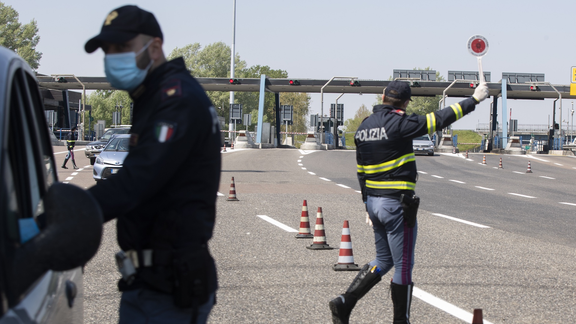 Police officers stop cars at the Melegnano highway barrier entrance, near Milan, Italy, Saturday, April 11, 2020. Using helicopters, drones and stepped-up police checks to make sure Italians don't slip out of their homes for the Easter holiday weekend, Italian authorities are doubling down on their crackdown against violators of the nationwide lockdown decree. (AP Photo/Luca Bruno)