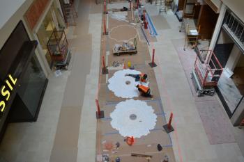 Jen Stark (lying on her side) and team member (kneeling) cut 3-D designs that complement the designs featured on an escalator