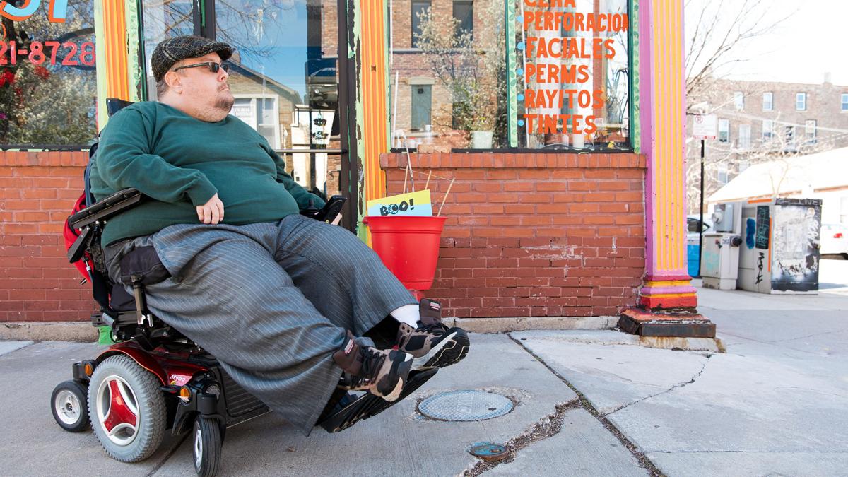 Adam Ballard is pictured on a cracked sidewalk in front of a beauty salon near his Pilsen home. (Michael Izquierdo / WTTW News)