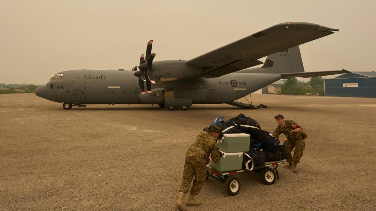 Royal Canadian Air Force Pte. Carter Brinn (left) and Cpl. Ethan Cai helps load cargo as evacuees from Pinaow Wachi Care Home board a C-130 Hercules aircraft in Norway House, Man., Tuesday, June 3, 2025, at the Norway House Airport as crews continue to fight wildfires in northern Manitoba. (David Lipnowski / The Canadian Press via AP)
