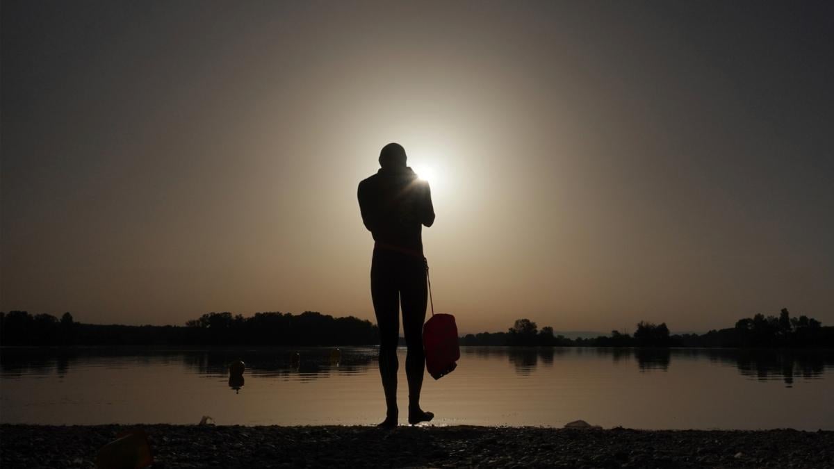 FILE - A man prepares to enter the water as the sun rises above the Miribel lake, outside Lyon, France, June 18, 2022. (Laurent Cipriani / AP Photo, File)