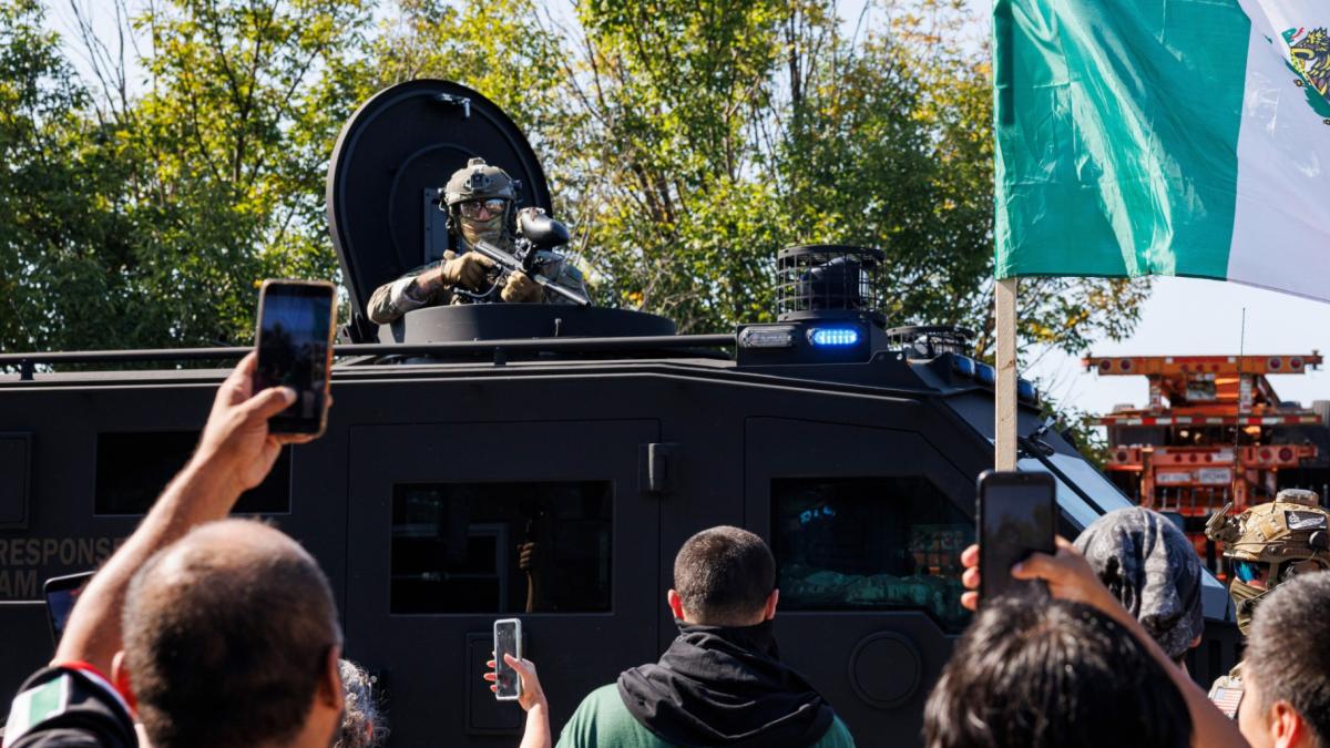 An ICE officer watches protestors as a Lenco BearCat vehicle drives to the scene in the Brighton Park neighborhood of Chicago, on Saturday, Oct. 4, 2025, after protesters learned that U.S. Border Patrol shot a woman Saturday morning on Chicago's Southwest Side. (Anthony Vazquez / Chicago Sun-Times via AP)
