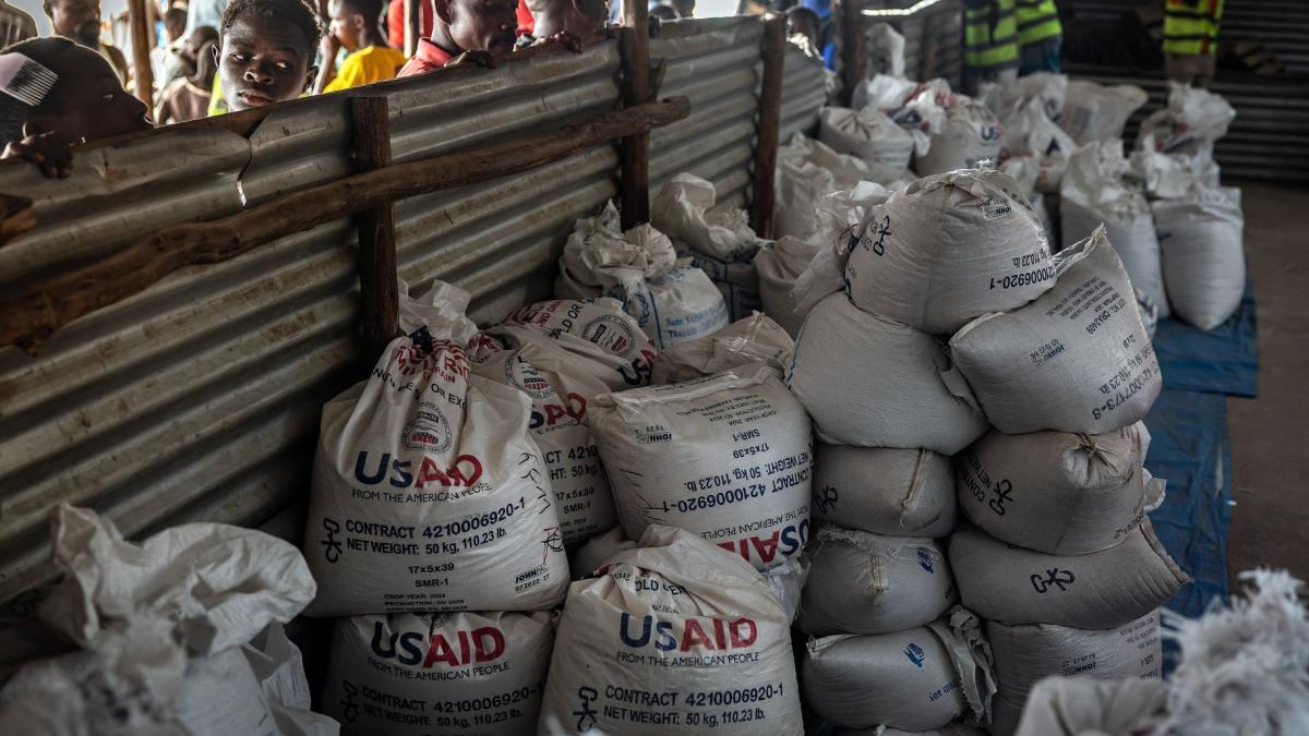 Congolese refugees look through a corrugated metal fence at the final batches of food delivered by the now-dismantled United States Agency for International Development (USAID) in a storage and food delivery area at the Musenyi refugee site in Giharo, on May 7, 2025. (Luis Tato / AFP / Getty Images via CNN Newsource)