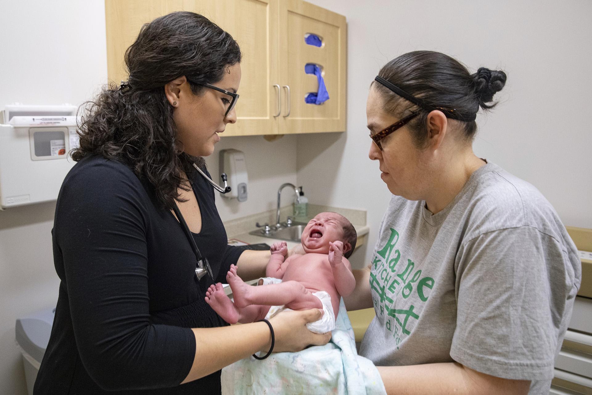 In this Aug. 13, 2019, photo, Dr. Jasmine Saavedra, left, a pediatrician at Esperanza Health Centers in Chicago, hands newborn Alondra Marquez to her mother, Esthela Nuñez, right, after examination. (AP Photo / Amr Alfiky)