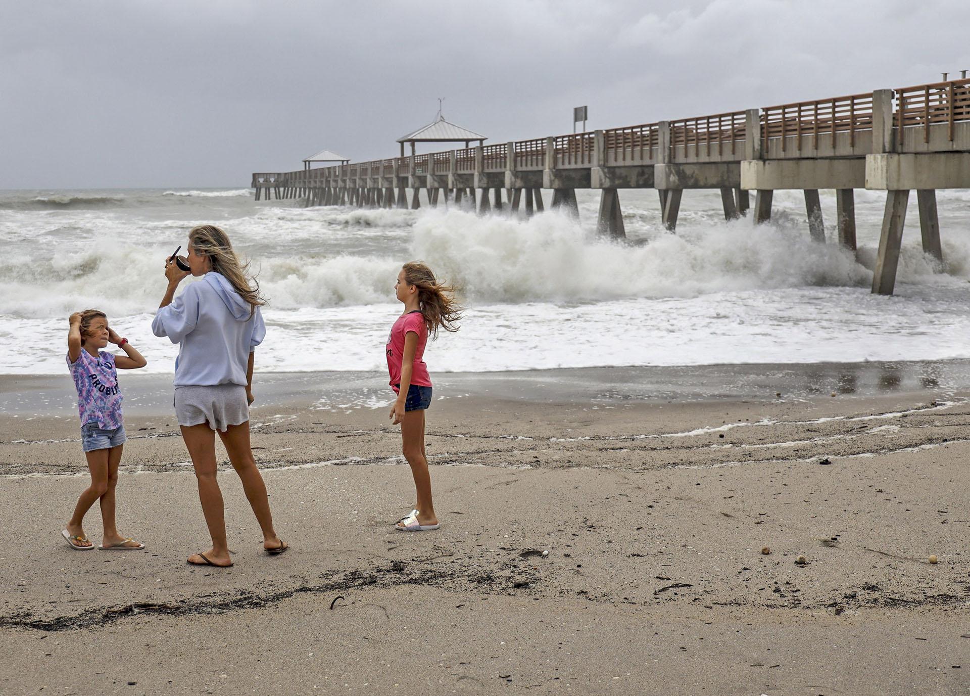 Juna Beach residents Anneka, 8, left, and sister, Breanna, 10, right, along with their mother, Leah Hanza, center, get a close look of the waves crashing against the Juno Beach Pier as Hurricane Dorian crawls toward Florida, and it continues to ravage the Bahamas on Monday, Sept. 2, 2019. (Carl Juste/Miami Herald via AP)