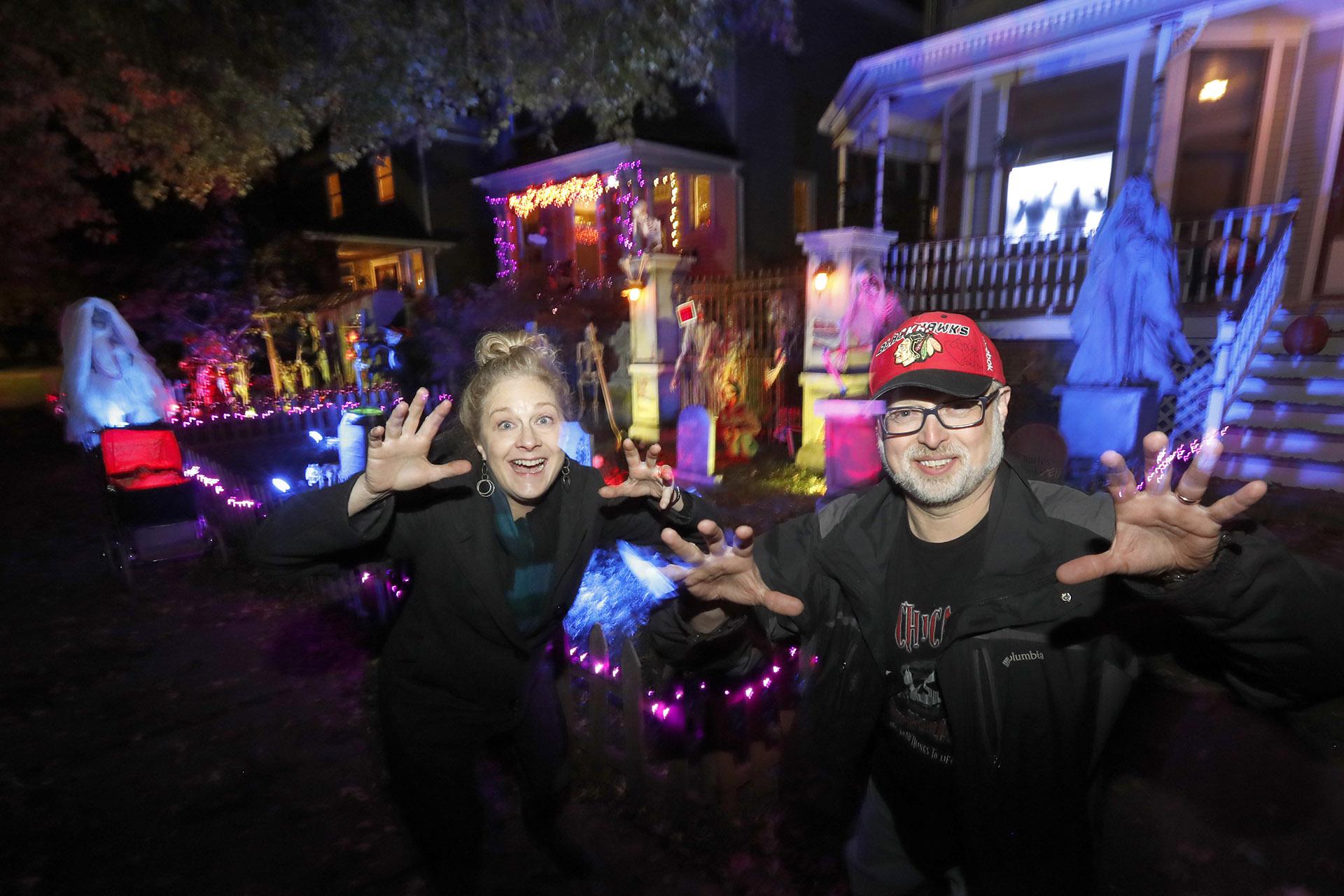 In this Tuesday, Oct. 29, 2019 photo, neighbors Beth LeFauve, left, and Nelson Gonzalez pose for a portrait outside their two Bernard Street homes and the Halloween decorations spanning both properties in Chicago. (AP Photo / Charles Rex Arbogast)