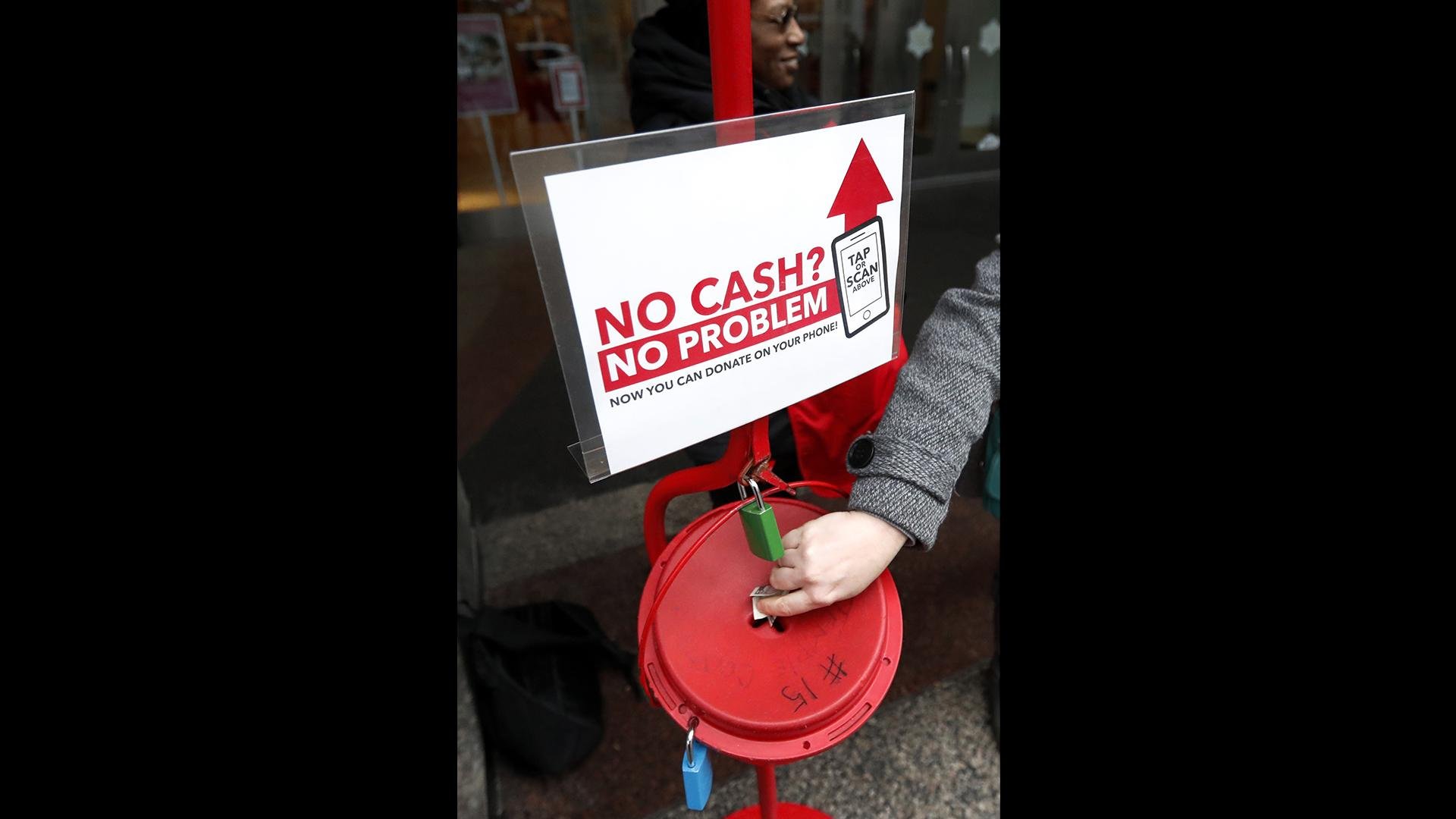 In this Friday, Nov. 15, 2019, photo, a shopper donates cash to the Salvation Army’s annual holiday red kettle campaign, with a reminder that mobile contributions are also accepted on Chicago’s Magnificent Mile. (AP Photo / Charles Rex Arbogast)