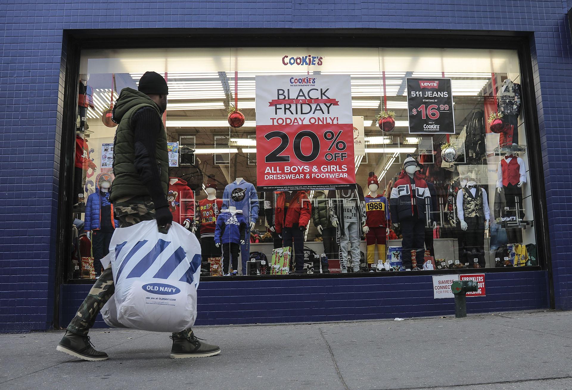 In this Nov. 29, 2019, file photo people walk by a Black Friday promotional at Cookie's department store in the Brooklyn Borough of New York. (AP Photo / Bebeto Matthews, File)
