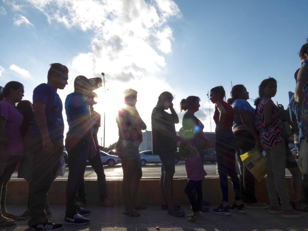 In this Oct. 5, 2019 file photo, migrants seeking asylum wait in line with their case paperwork during a weekly trip by volunteers, lawyers, paralegals and interpreters to the migrant campsite outside El Puente Nuevo in Matamoros, Mexico. (Denise Cathey / The Brownsville Herald via AP, File)