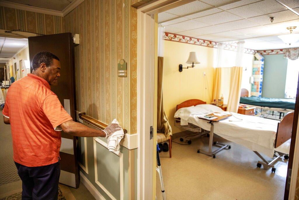 In this March 6, 2020, photo, Guilherme Gomes sanitizes a handrail at the South Shore Rehabilitation and Skilled Care Center, in Rockland, Mass. Staff at the 96-bed nursing home held an informational meeting for residents and have been stockpiling supplies, stepping up their daily disinfection routine and screening visitors for potential illness in recent days. (AP Photo / David Goldman)