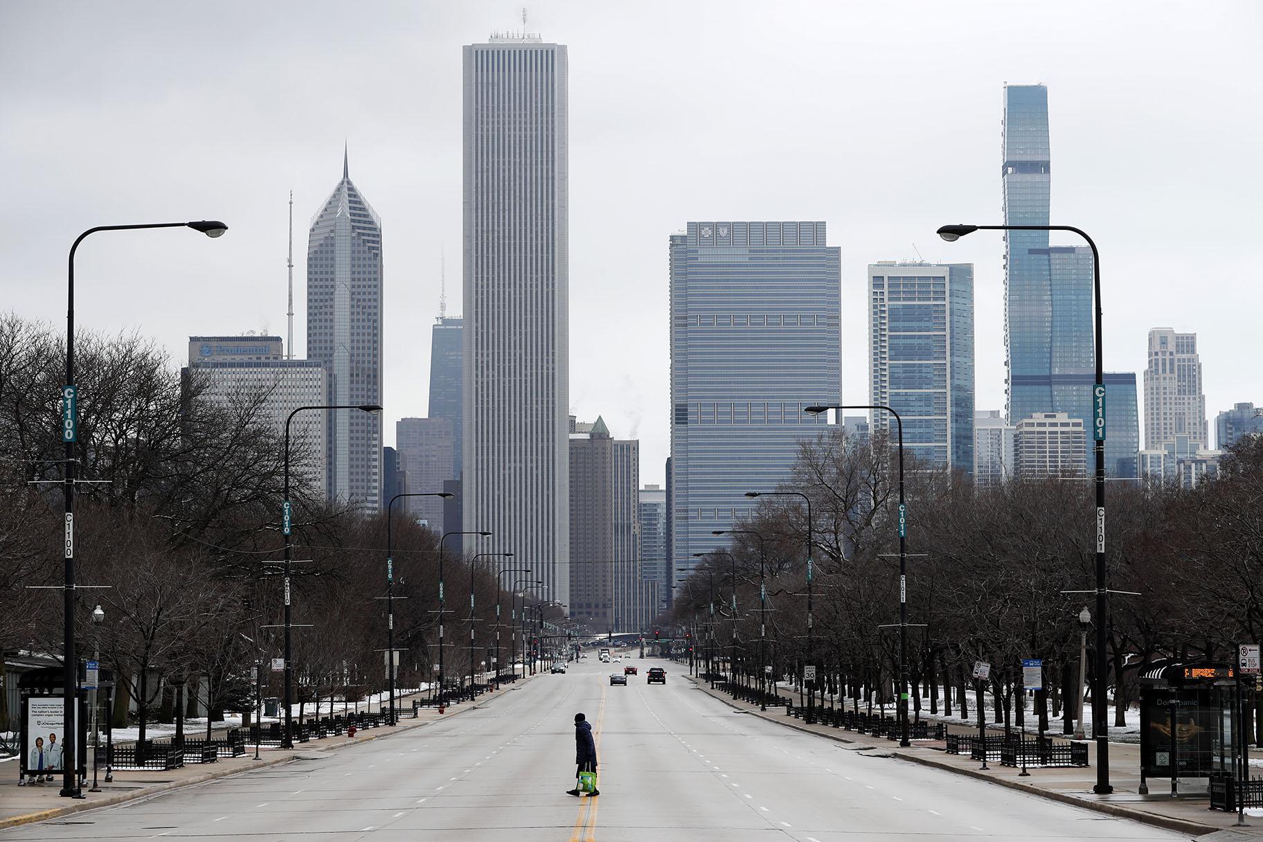 An elderly woman walks across the usually busy Columbus Drive that splits Chicago’s Grant Park in half, on the first work day since Illinois Gov. J.B. Pritzker gave a shelter in place order last week, Monday, March 23, 2020, photo, in Chicago. (AP Photo / Charles Rex Arbogast)