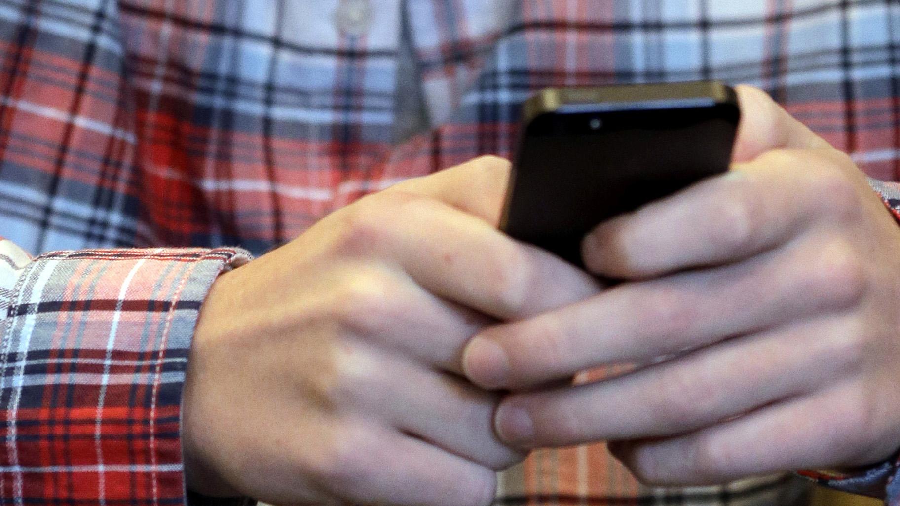 In this Oct. 24, 2013, file photo, a person checks their smartphone in Glenview, Ill. A mysterious wave of texts swept America’s phones overnight Wednesday, Nov. 6, 2019, delivering unintelligible messages that left many people mildly confused when they woke up on Thursday. (AP Photo / Nam Y. Huh, File)