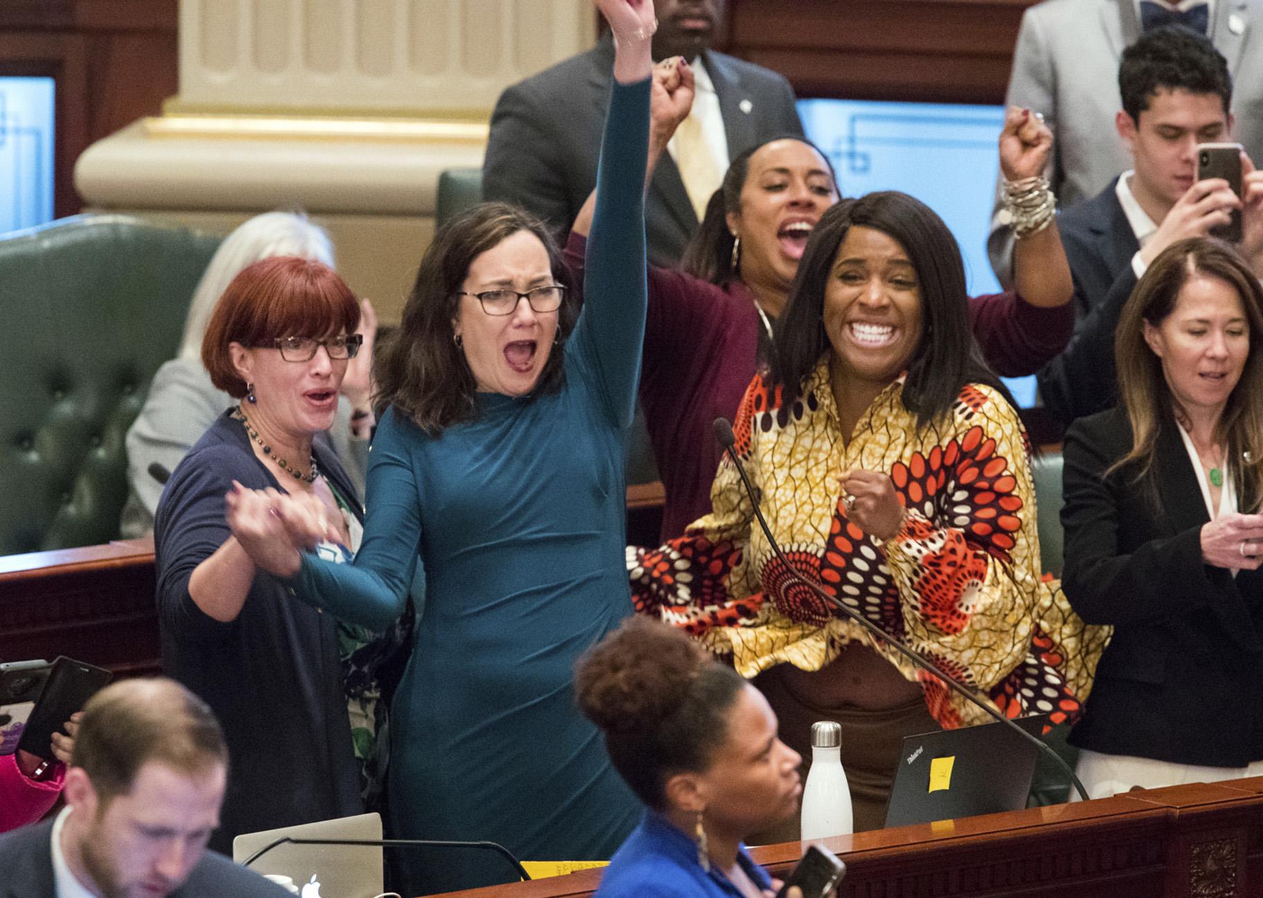 Illinois state Rep. Kelly Cassidy, D-Chicago, throws her fist in the air as she celebrates with Illinois state Sen. Heather Steans, D-Chicago, left, and Rep. Jehan Gordon-Booth, D-Peoria, as they watch the final votes come in for their bill to legalize recreational marijuana use in the Illinois House chambers Friday, May 31, 2019. The 66-47 vote sends the bill to Gov. J.B. Pritzker who indicated he will sign it. (Ted Schurter / The State Journal-Register via AP)