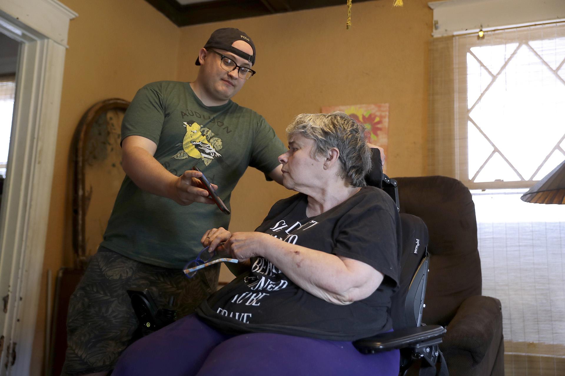 In this Tuesday, April 28, 2020, photo Zach Stafford, left, shows his mother, Debra Mize, a news alert on his phone as they watch a livestream of the daily coronavirus briefing by Illinois Gov. J.B. Pritzker on a television just out of view inside their home in Belleville, Illinois. (AP Photo / Jeff Roberson)