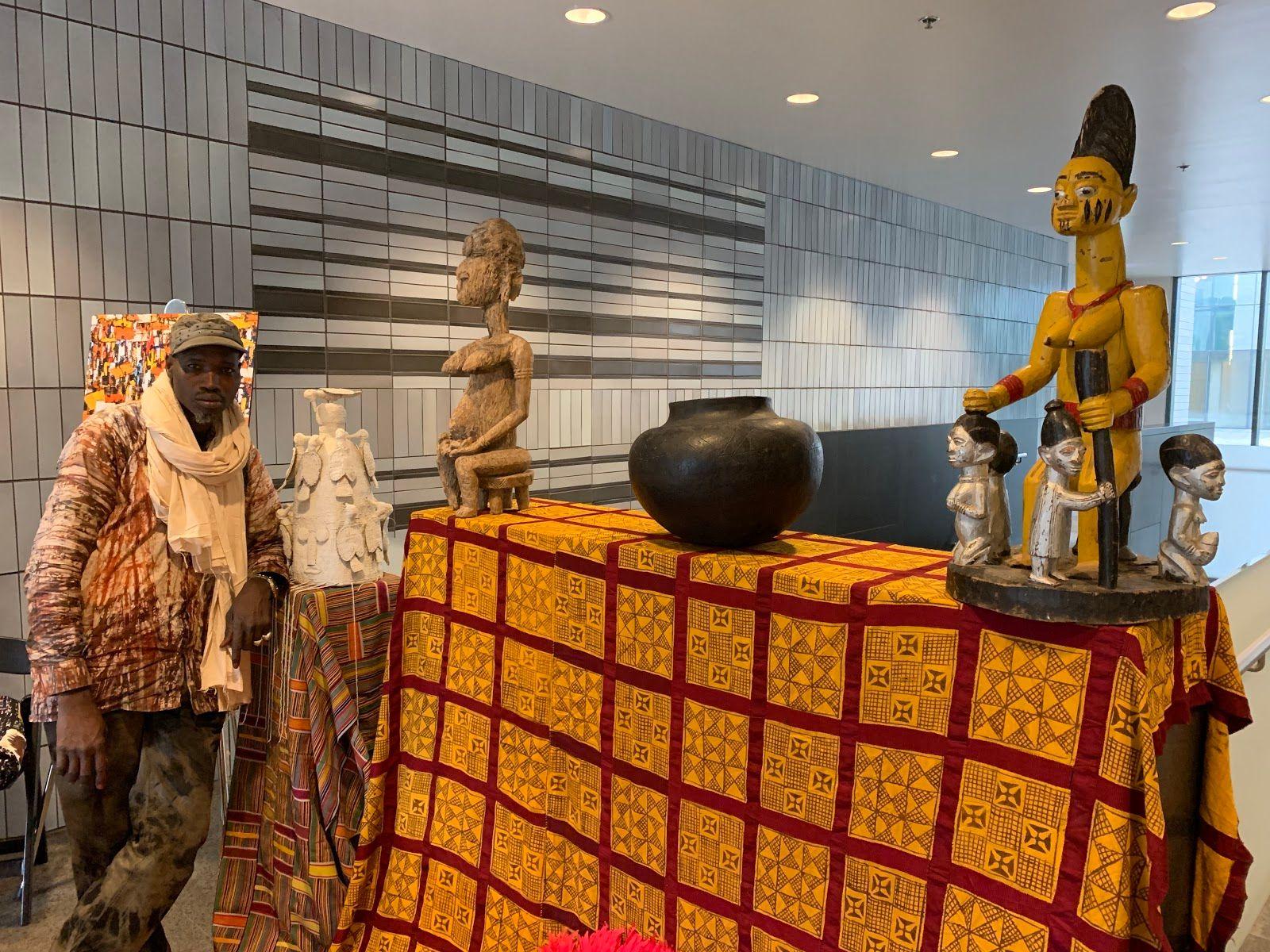 Diarra Diaby stands next to collected pieces. From left: a ceremonial Yoruba crown, “Mother and Son” statue, South African cooking pot and “Queen Mother” statue. (Angel Idowu / WTTW News)