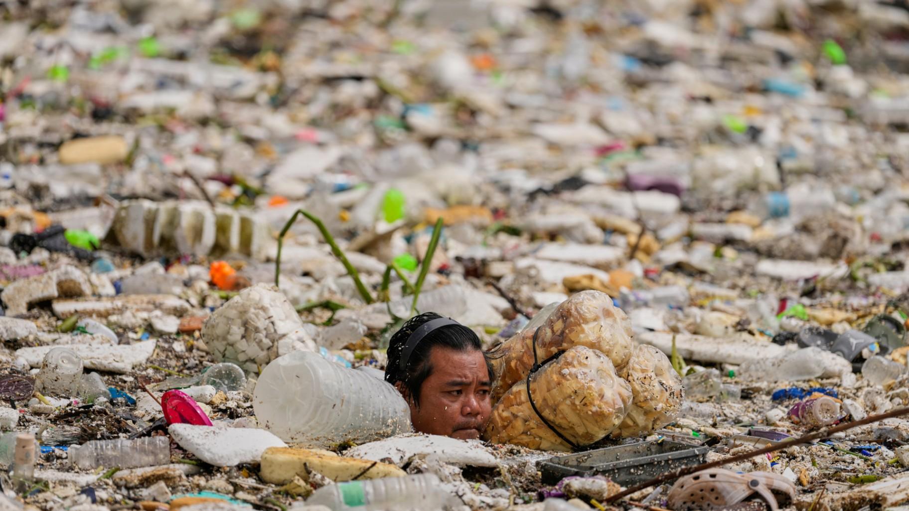 A worker uses improvised floats while trying to clear a sea of garbage and debris brought by intense monsoon rains at the Redemptorist Water Channel in Paranaque city, Metro Manila, Philippines, Aug. 11, 2026. (AP Photo / Aaron Favila, File)