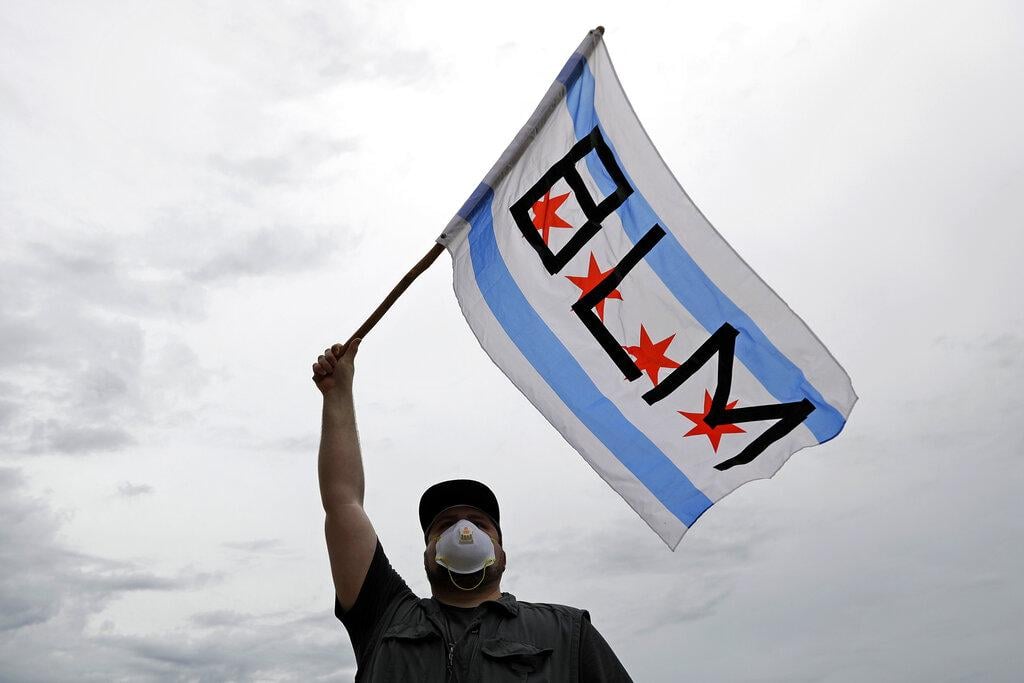 In this June 3, 2020, file photo, a protester waves a city of Chicago flag emblazoned with the acronym BLM for Black Lives Matter, outside the Batavia, Ill., City Hall during a protest over the death of George Floyd. (AP Photo / Nam Y. Huh, File)