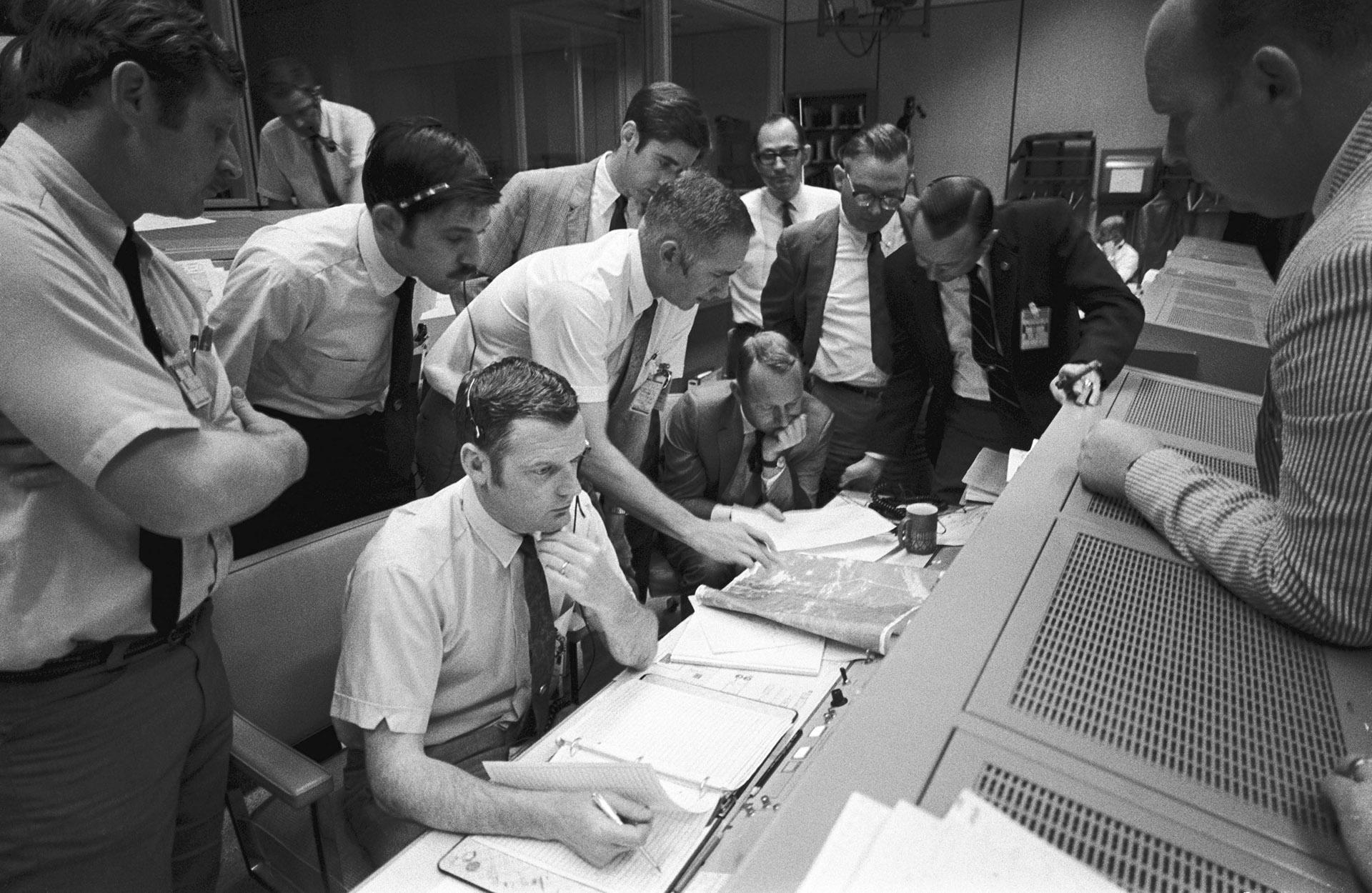 In this April 15, 1970 photo made available by NASA, a group of flight controllers gather around the console of Glenn S. Lunney, foreground seated, Shift 4 flight director, in the Mission Operations Control Room of Mission Control Center in Houston. Their attention is drawn to a weather map of the proposed landing site in the Pacific Ocean. At this point, the Apollo 13 lunar landing mission had been canceled, and the problem-plagued Apollo 13 crew members were in trans-Earth trajectory attempting to bring t