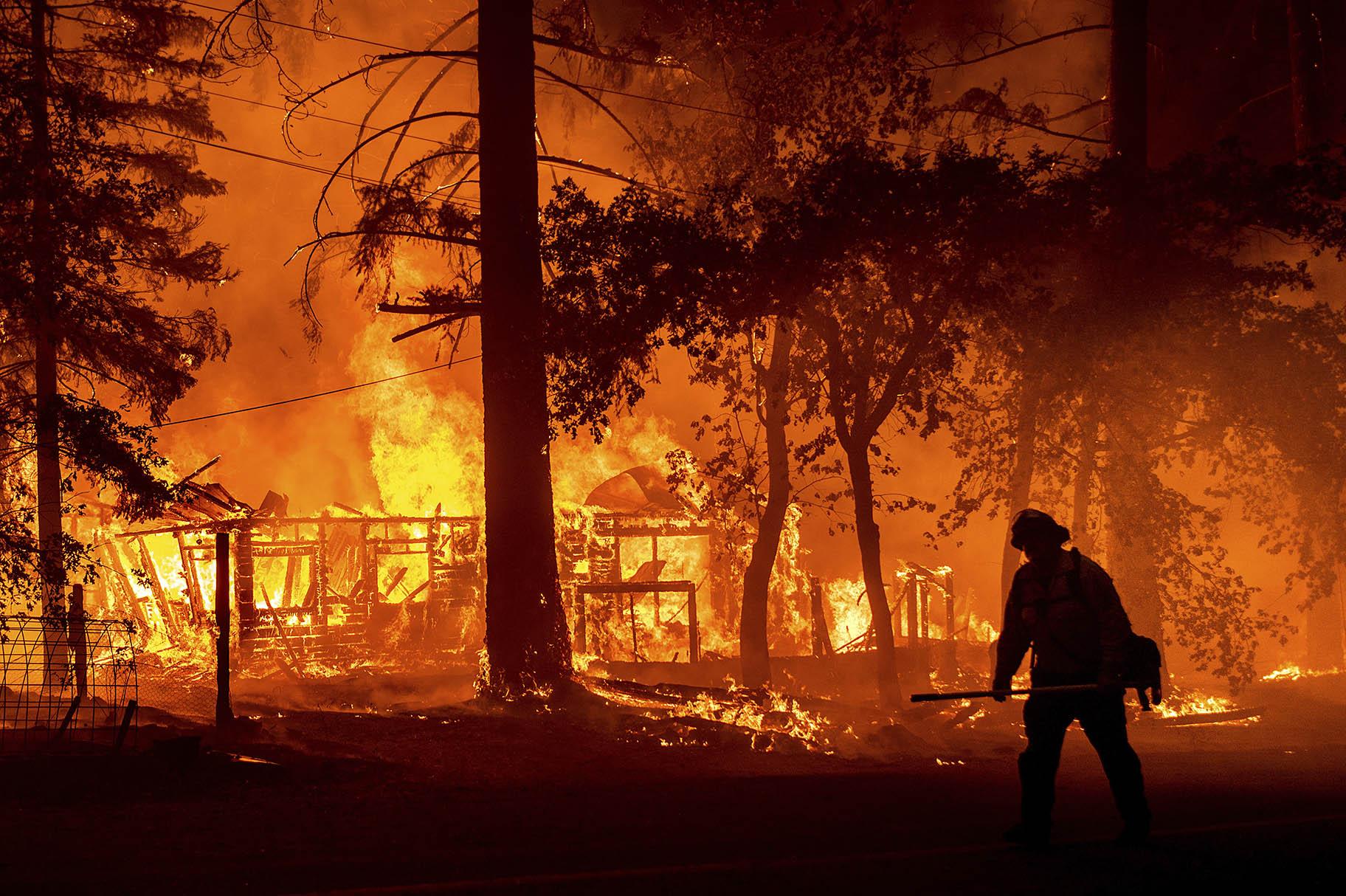 In this Saturday, July 24, 2021, file photo a firefighter passes a burning home as the Dixie Fire flares in Plumas County, Calif. (AP Photo / Noah Berge, File)