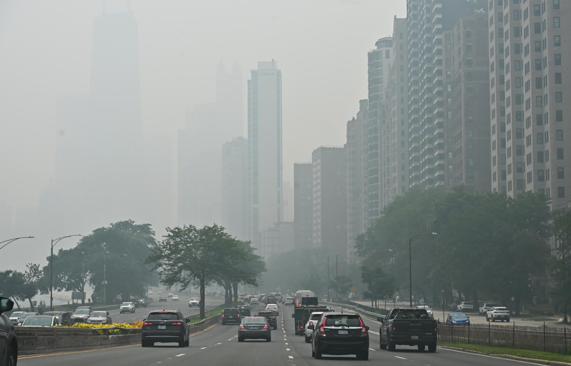 The iconic John Hancock Center is reduced to a faint silhouette behind a thick shroud of Canadian wildfire smoke as vehicles head southbound on DuSable Lake Shore Drive near the Gold Coast neighborhood on Thursday, July 16, 2026. (Victor Hilitski / WTTW News)