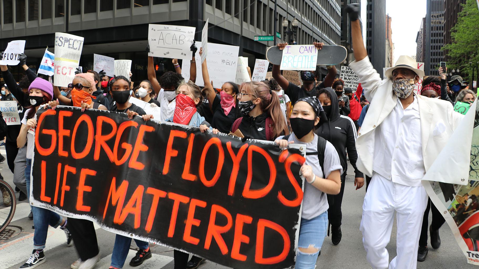 Protesters march along Dearborn Street while holding a sign honoring George Floyd on Saturday, May 30, 2020. Eric Russell, right, an activist with the Tree of Life Justice League, joins them. He also spoke at the protest. (Evan Garcia / WTTW News)