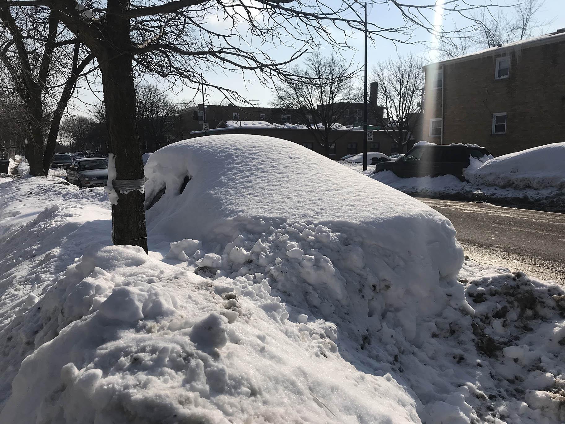 A car parked on a street in Chicago is buried by snow from recent storms. Sunshine and warmer temperatures on Saturday, Feb. 20, 2021 melted some snow, but there is still plenty to shovel. (WTTW News)