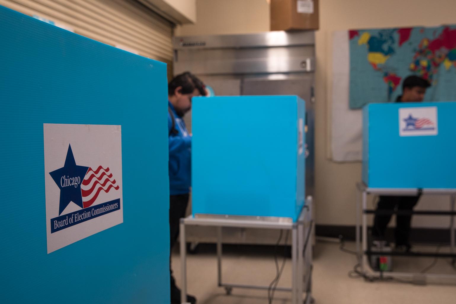 Two seniors from Kelvyn Park High School fill out their ballots for the Feb. 28 Chicago municipal election behind voting booths at the Kilbourn Park polling station. (Michael Izquierdo / WTTW News)