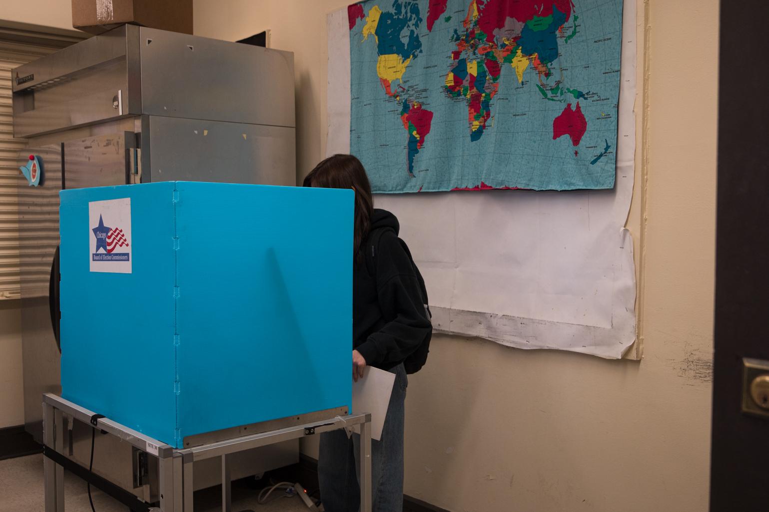 A senior from Kelvyn Park High School fills out their ballot for the Feb. 28 Chicago municipal election behind a voting booth at the Kilbourn Park polling station. (Michael Izquierdo / WTTW News)