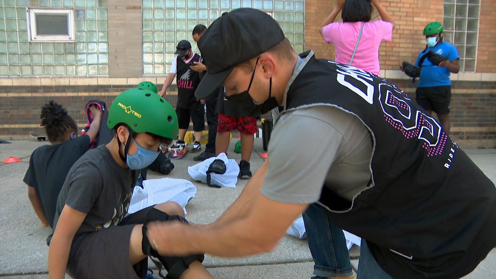 An instructor straps protective knee pads onto a participant of the Chill Foundation’s spring skateboard program at Louis L. Valentine Boys & Girls Club on May 26, 2021. (WTTW News)
