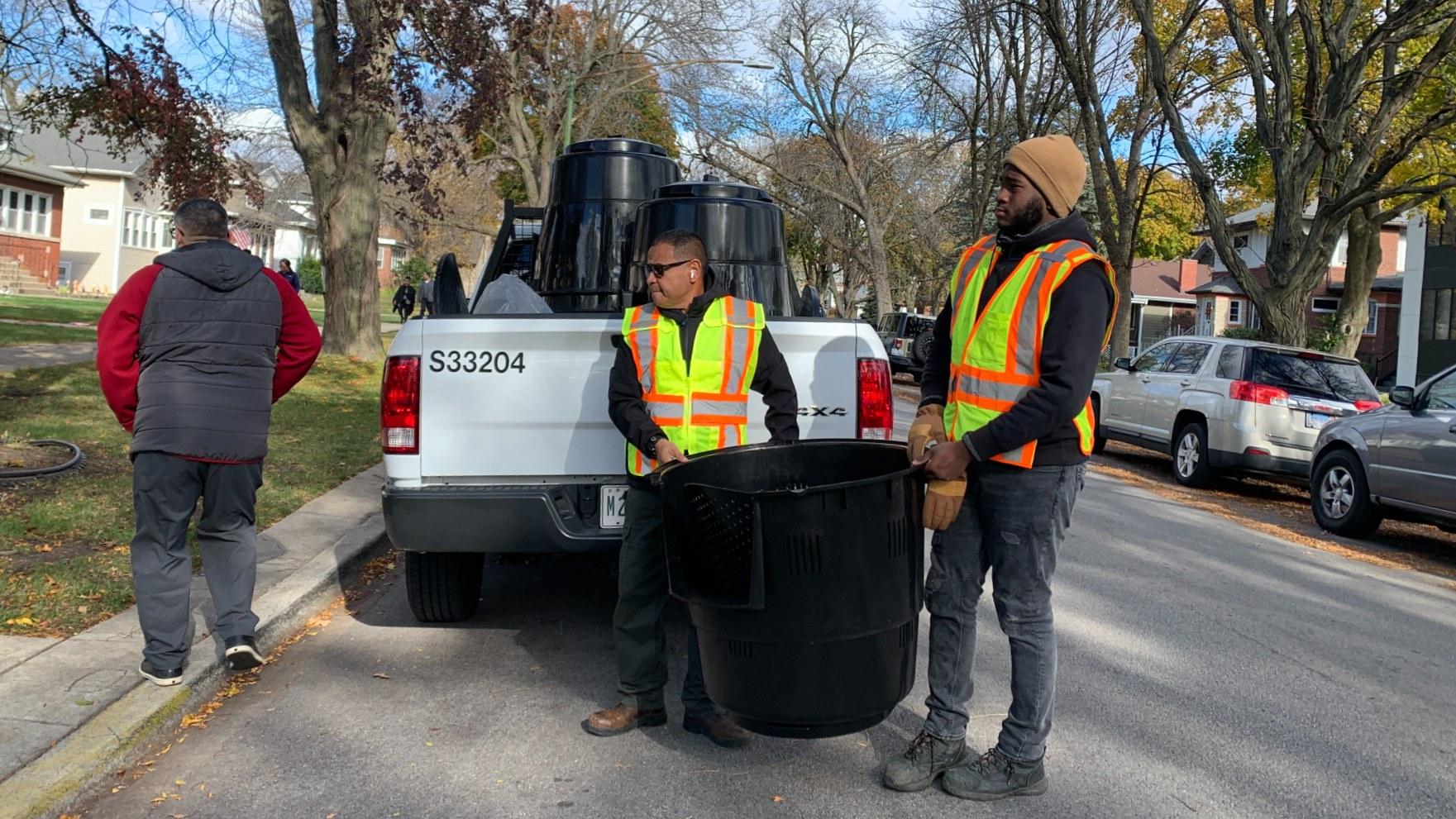  Streets and Sanitation Ward Superintendent Carlos Cintron, left, and Streets and Sanitation laborer Jaden Bishop carry a backyard compost bin from their truck to deliver to a resident on the Northwest Side on Nov. 12, 2024. (Eunice Alpasan / WTTW News)