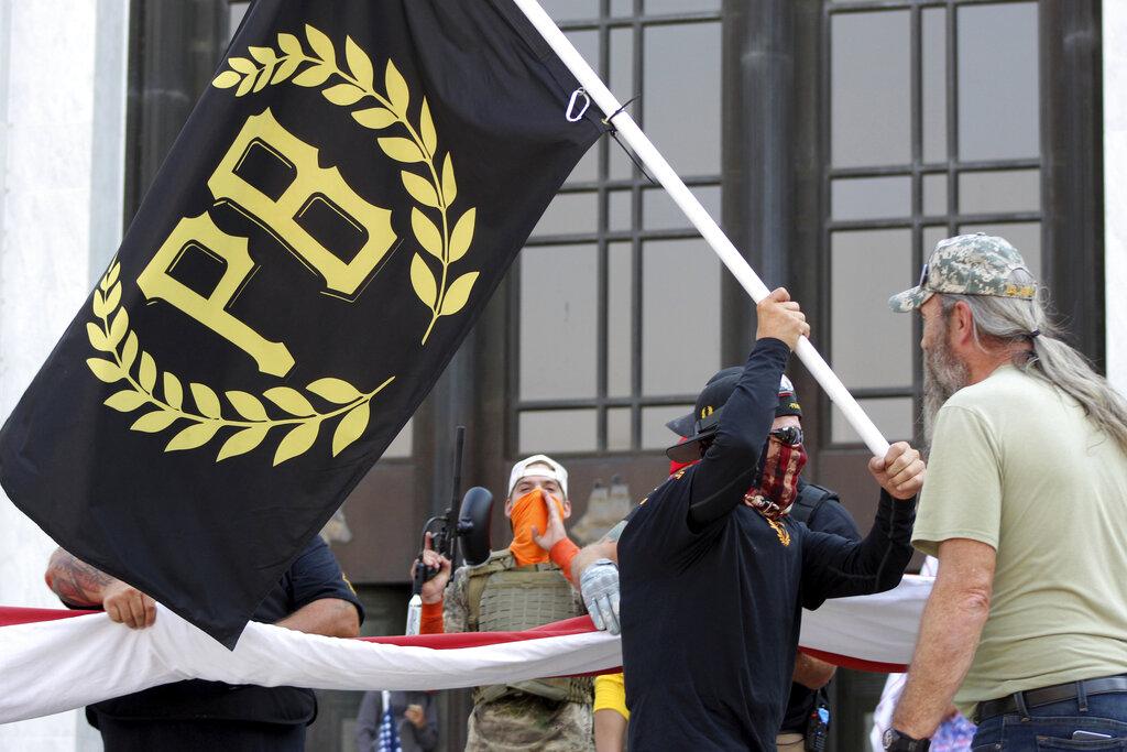In this Sept. 7, 2020 photo, a protester carries a Proud Boys banner, symbol of a right-wing group, while other members start to unfurl a large U.S. flag in front of the Oregon State Capitol in Salem, Ore. (AP Photo / Andrew Selsky, File)