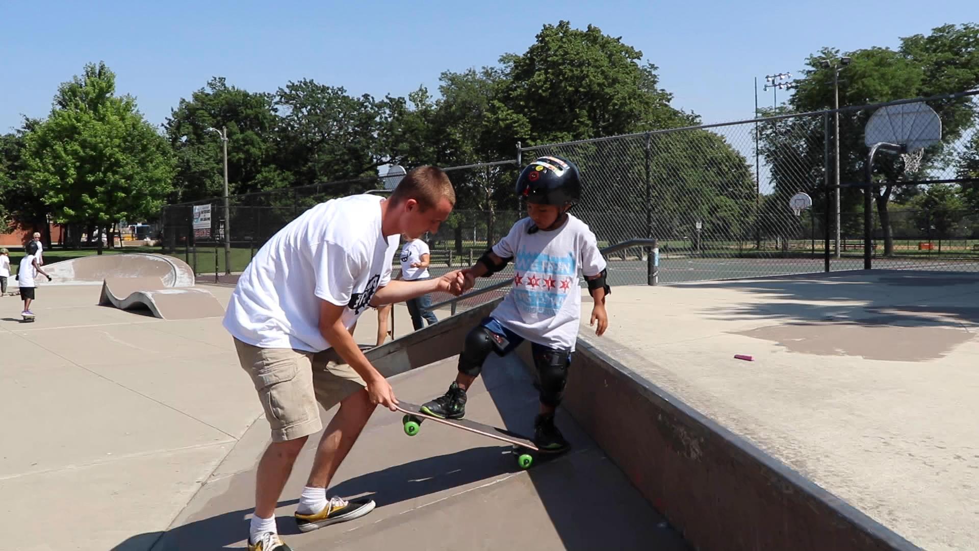 Skate instructor Grant Katula helps a young skater “drop in” on a ramp at Piotrowksi Skate Park. (Evan Garcia / WTTW News)