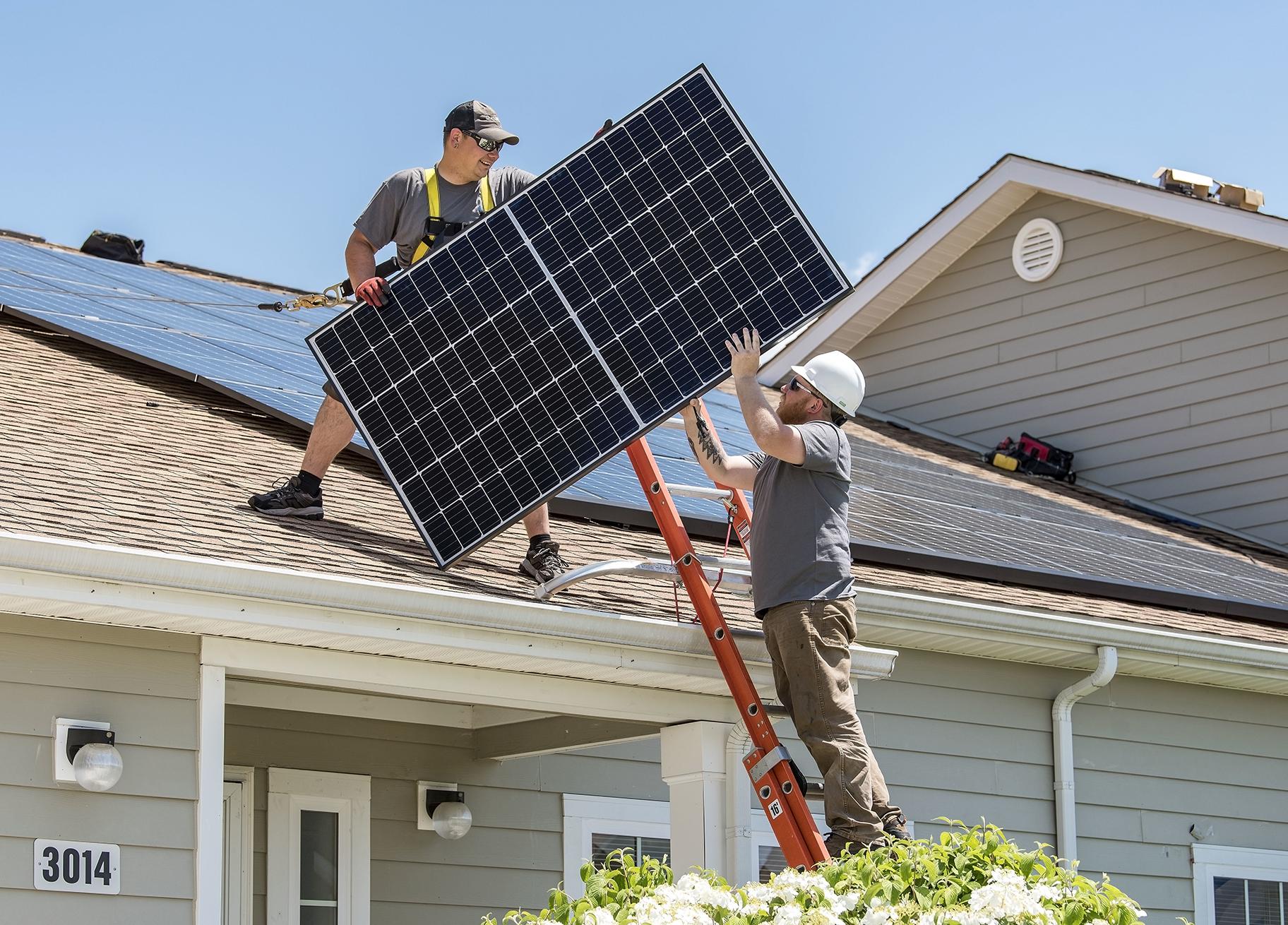 Wyatt Whelan, left, and Eric Roberts move a photovoltaic panel to a roof on May 11, 2018, in the Dover Family Housing community at Dover Air Force Base in Delaware. (Roland Balik / U.S. Air Force) 