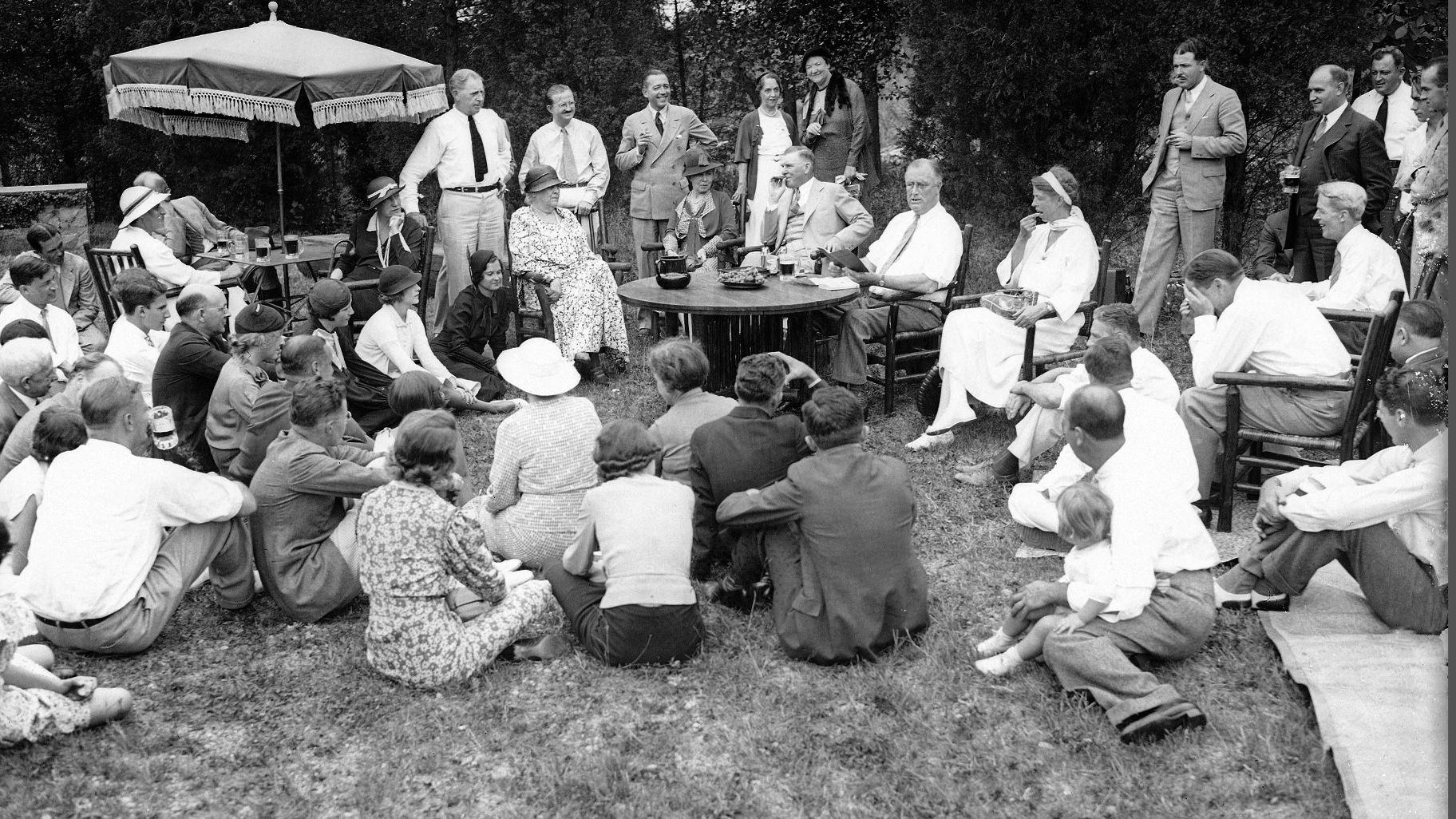 President Franklin Roosevelt reads to his guests as he and first lady Eleanor Roosevelt, at table, host a Labor Day picnic at their residence in Hyde Park, N.Y., Sept. 3, 1934. (AP Photo, File)
