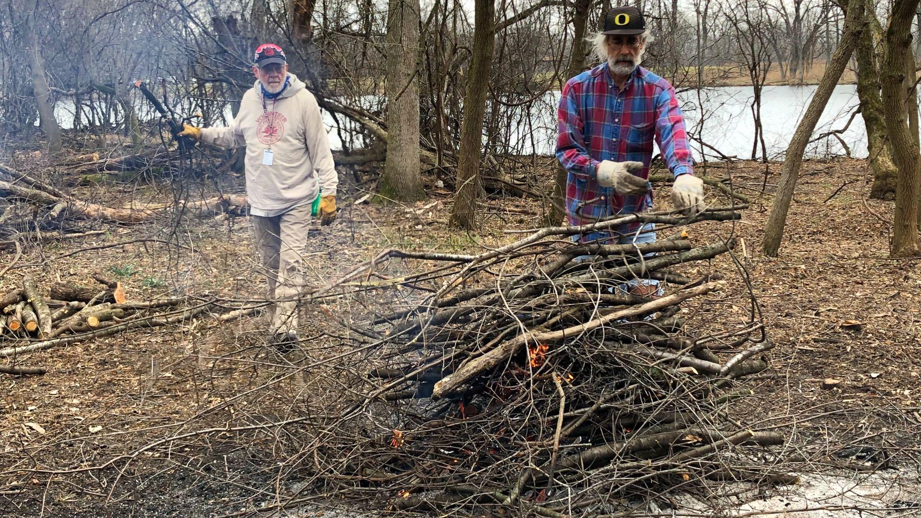 Long-time volunteers Gary Morrissey and Dan Goodwin stoke the pile of burning buckthorn. (Patty Wetli / WTTW News)