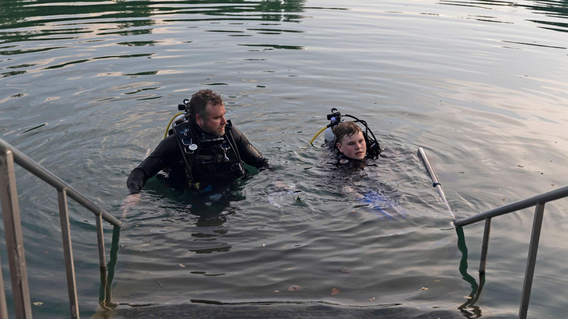 Allen Jones looks toward his son Adrian Jones, who is taking off his fins before stepping out of the Mermet Springs quarry on July 17, 2026, at Mermet Springs in Belknap, Illinois. The father and son got certified together almost a year ago. (Peyton Cook / Saluki Local Reporting Lab)