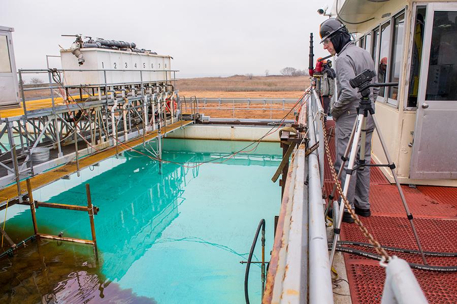 Argonne scientist Seth Darling, who co-invented the material, watches as the Oleo Sponge collects dark brown oil from the water during tests at Ohmsett in New Jersey. (Mark Lopez / Argonne National Laboratory)