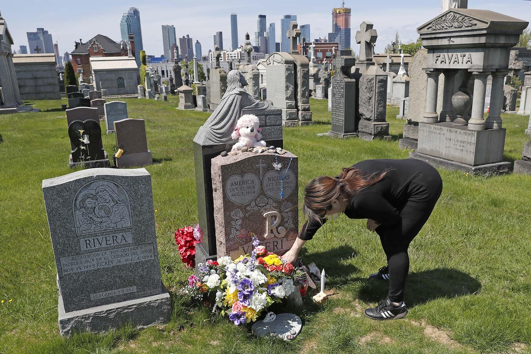 In this Sunday, May 10, 2020 file photo, Sharon Rivera adjusts flowers and other items left at the grave of her daughter, Victoria, at Calvary Cemetery in New York, on Mother’s Day. (AP Photo / Kathy Willens, File)