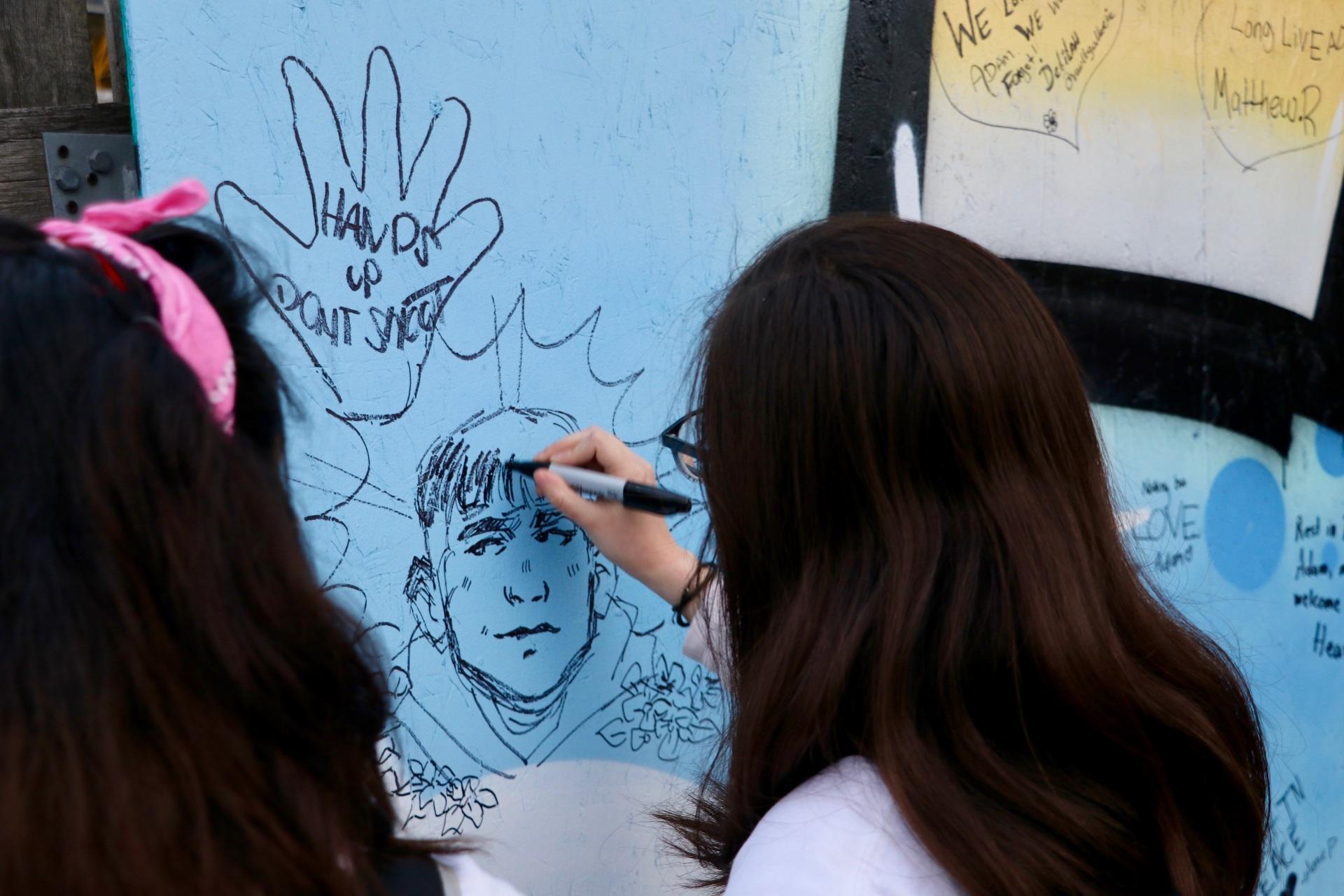 During a peace walk in honor of Adam Toledo on April 18, 2021, an attendee draws a portrait of 13-year-old Adam Toledo on a mural near where Toledo was fatally shot by a police officer on March 29, 2021. (Evan Garcia / WTTW News)