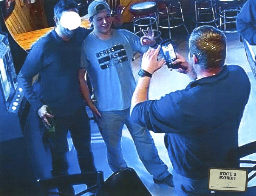 In this image from video provided by the Kenosha County District Attorney, Kyle Rittenhouse poses for a photo at Pudgy's Pub in Mount Pleasant, Wis., on Jan. 5, 2021, the day he was arraigned on charges related to the killing of two people at an August protest in Kenosha. (Courtesy of Kenosha County District Attorney via AP)