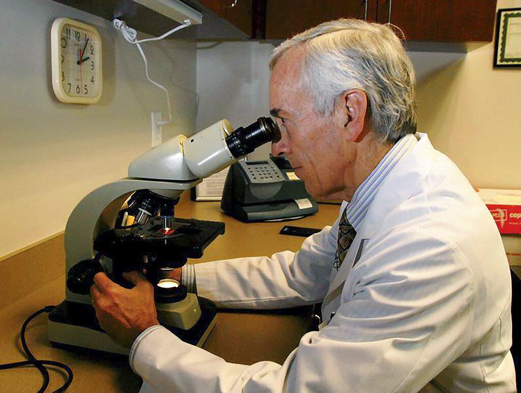 In this undated photo provided by Atlanta Allergy & Asthma, Dr. Stanley Fineman looks through a microscope at Atlanta Allergy & Asthma Center in Atlanta to examine pollen. (Robin B. Panethere / Atlanta Allergy & Asthma via AP)