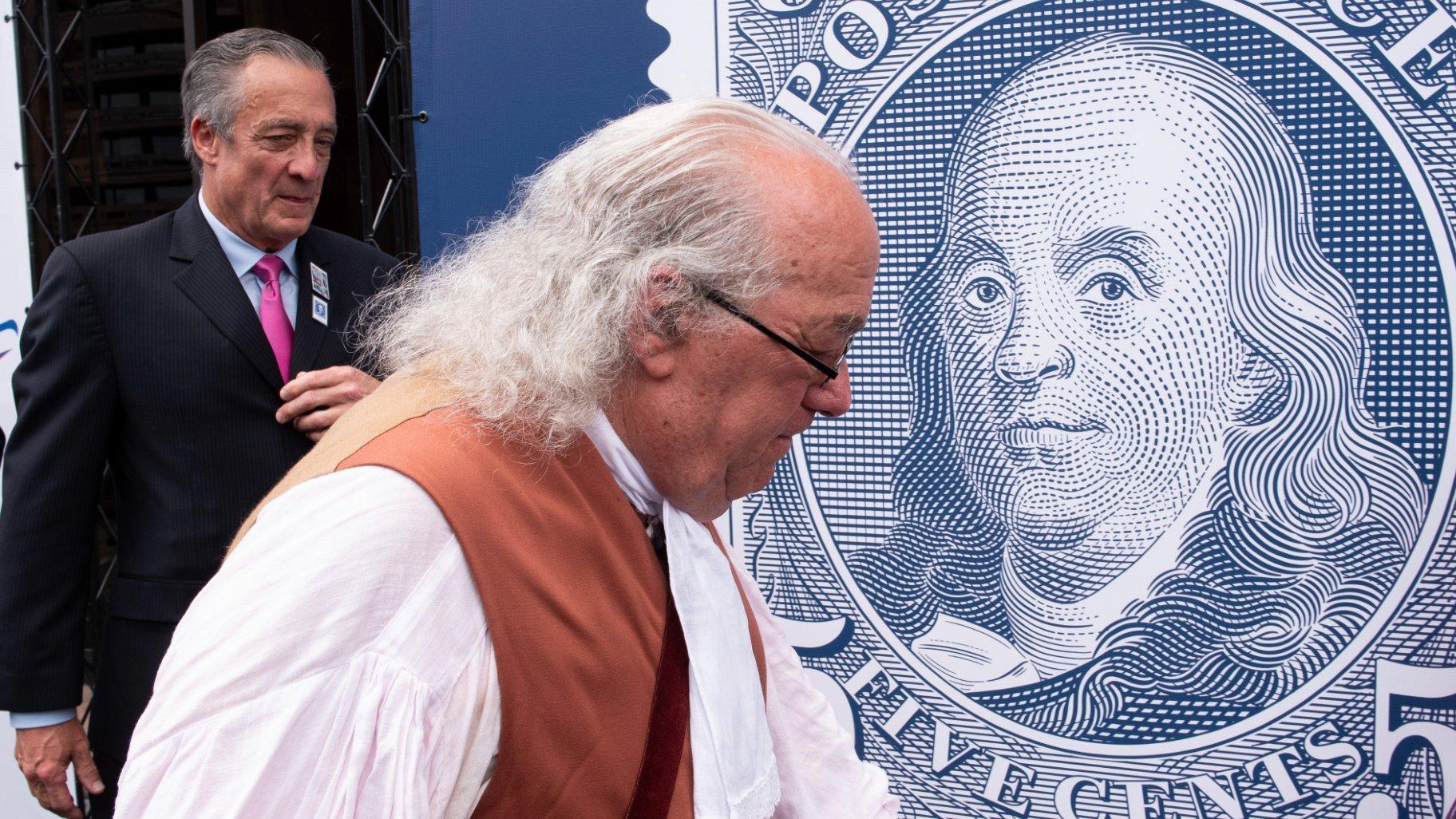 FILE - Barry Stevens, portraying Benjamin Franklin, right, walks past a just unveiled stamp marking the 250th anniversary of the postal service, Wednesday, July 23, 2025, in Washington, as Postmaster General David Steiner looks on. (AP Photo / Cliff Owen, File)