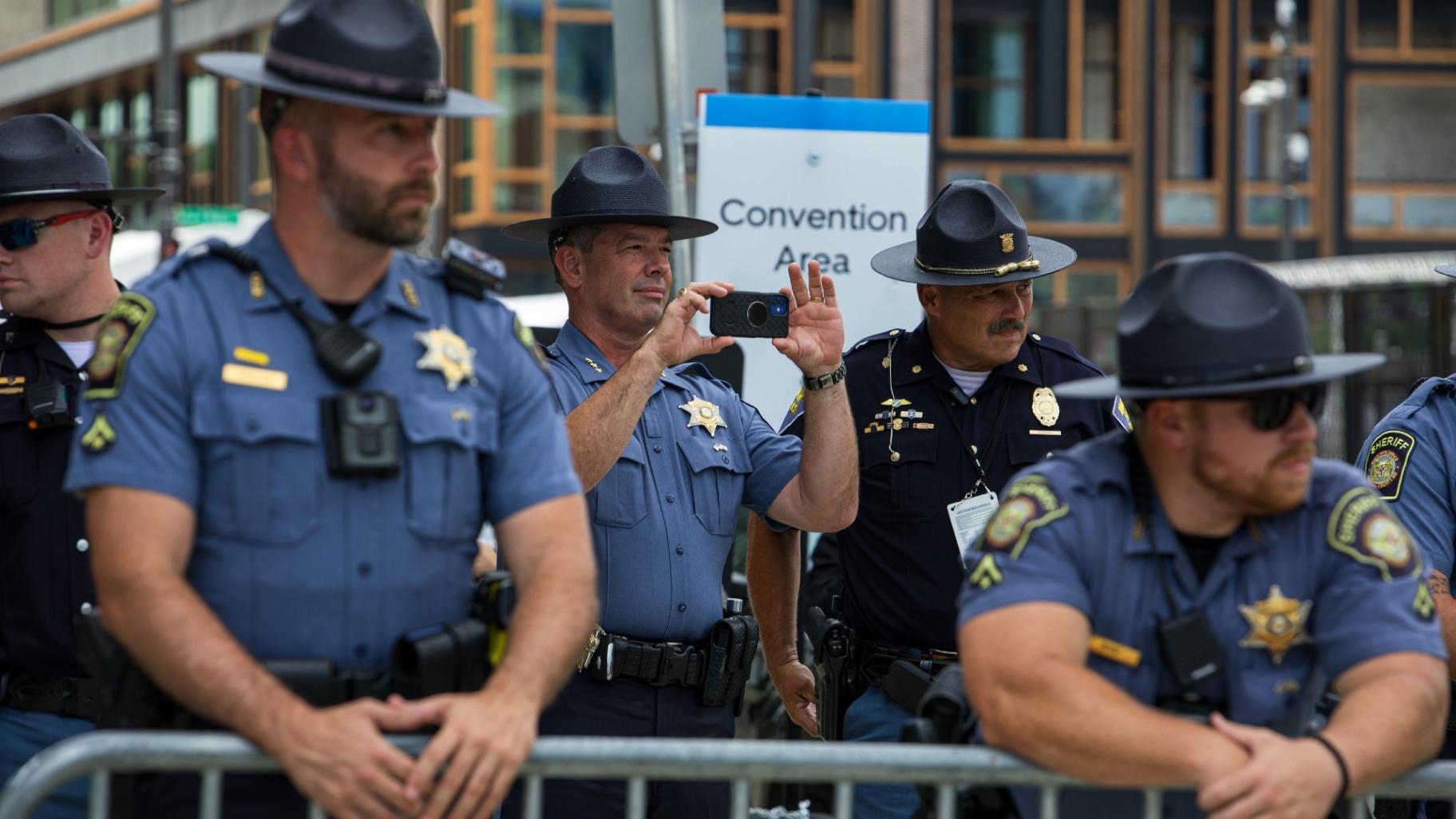 Police officers gathered outside the convention area watch and record on their phones as protestors march in downtown Milwaukee on Monday, July 15, 2024. (Michael Izquierdo / WTTW News)