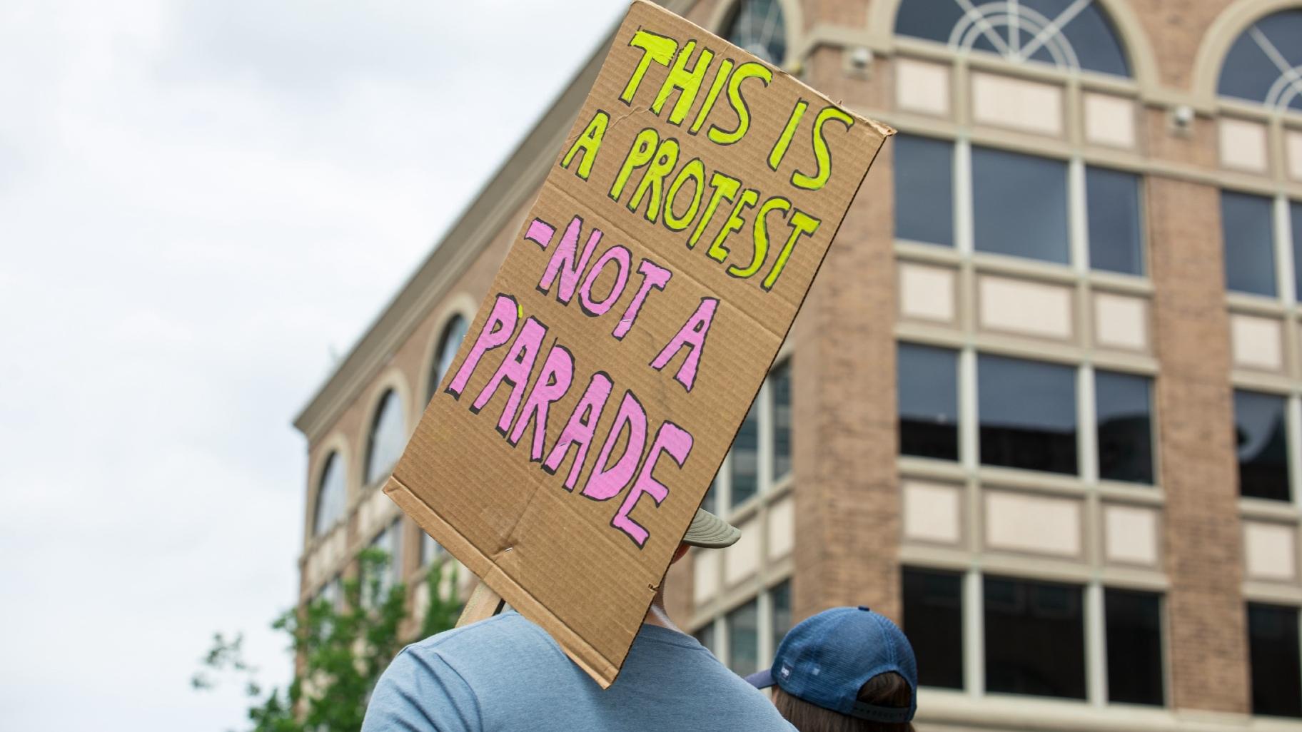 A protester holds up a sign reading “This is a protest, not a parade” in downtown Milwaukee on Monday, July 15, 2024. (Michael Izquierdo / WTTW News)