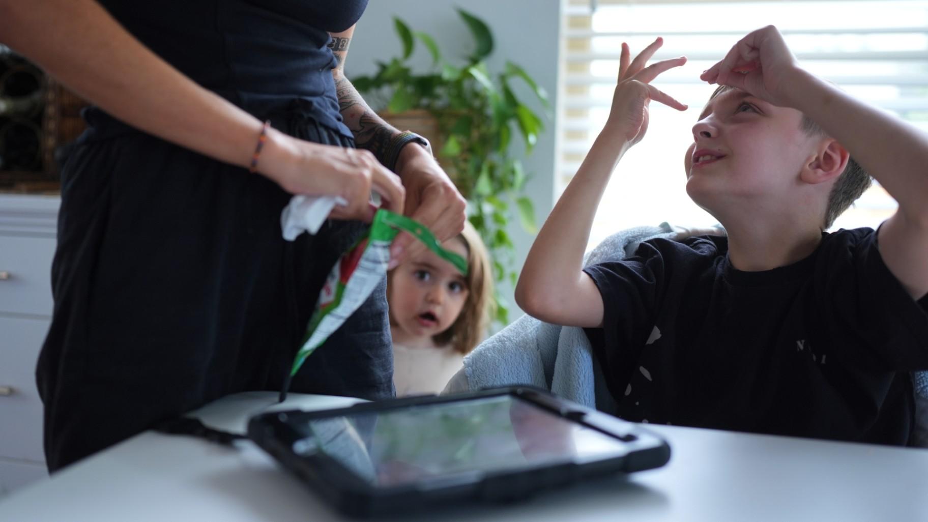 Charlie Lamb, right, who is diagnosed with autism and is non-verbal, uses an AAC device to communicate with his mother Eileen Lamb left, who also has autism, as Charlie's sister Billie looks on, Monday, May 12, 2025, in Austin, Texas. (AP Photo / Eric Gay)