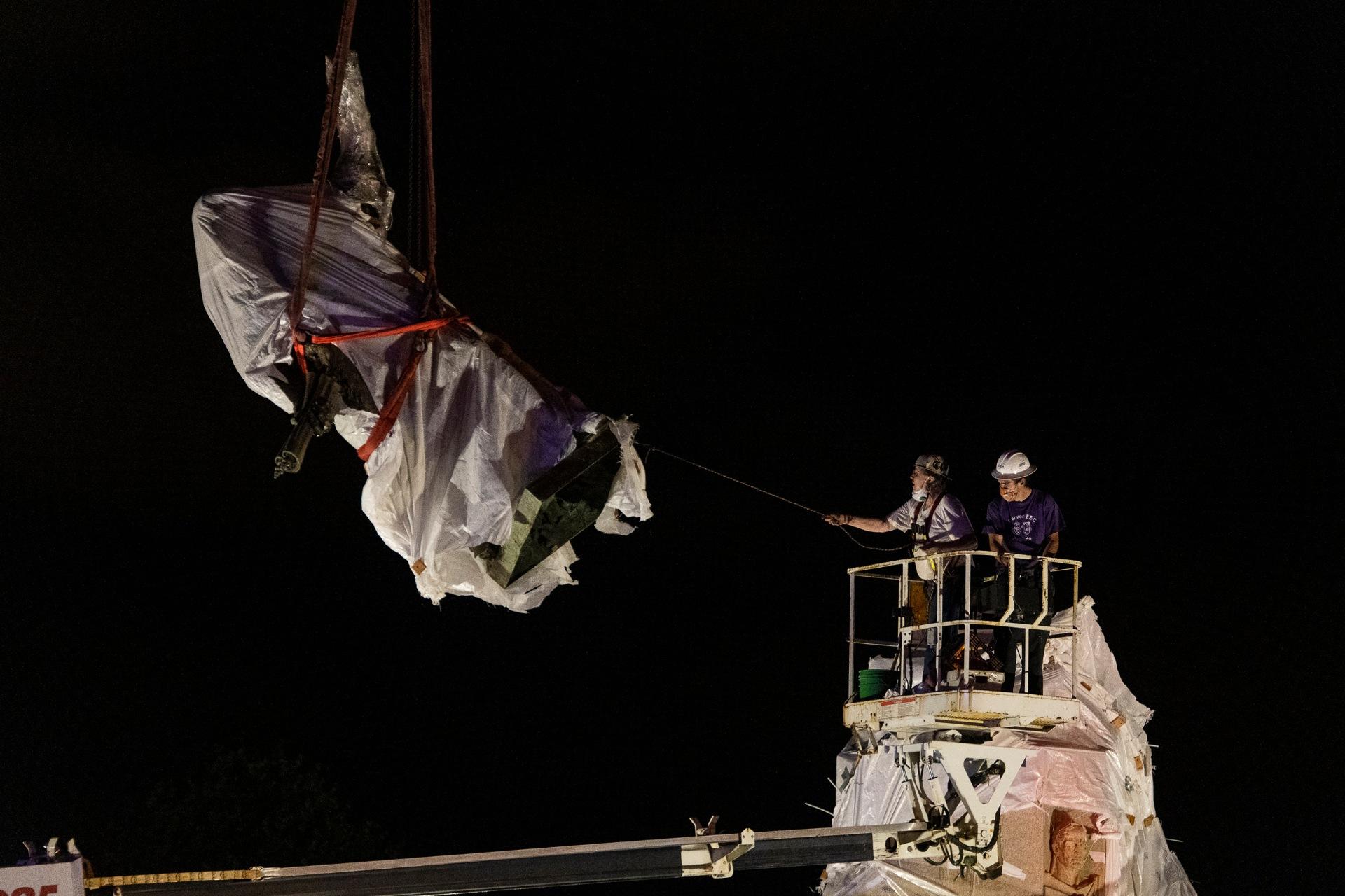 City municipal crews help guide the Christopher Columbus statue in Grant Park as it is removed by a crane, Friday, July 24, 2020, in Chicago. A statue of Christopher Columbus that drew chaotic protests in Chicago was taken down early Friday amid a plan by President Donald Trump to dispatch federal agents to the city. (Tyler LaRiviere / Chicago Sun-Times via AP)