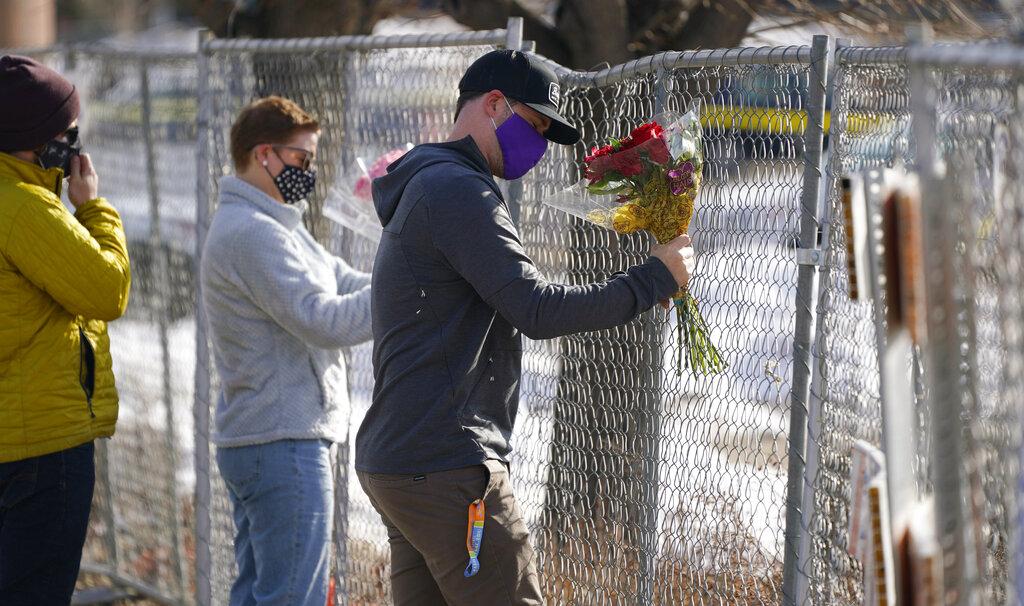 Kiefer Johnson places a bouquet of flowers into a makeshift fence put up around the parking lot outside a King Soopers grocery store where a mass shooting took place a day earlier, in Boulder, Colo., Tuesday, March 23, 2021. (AP Photo / David Zalubowski)
