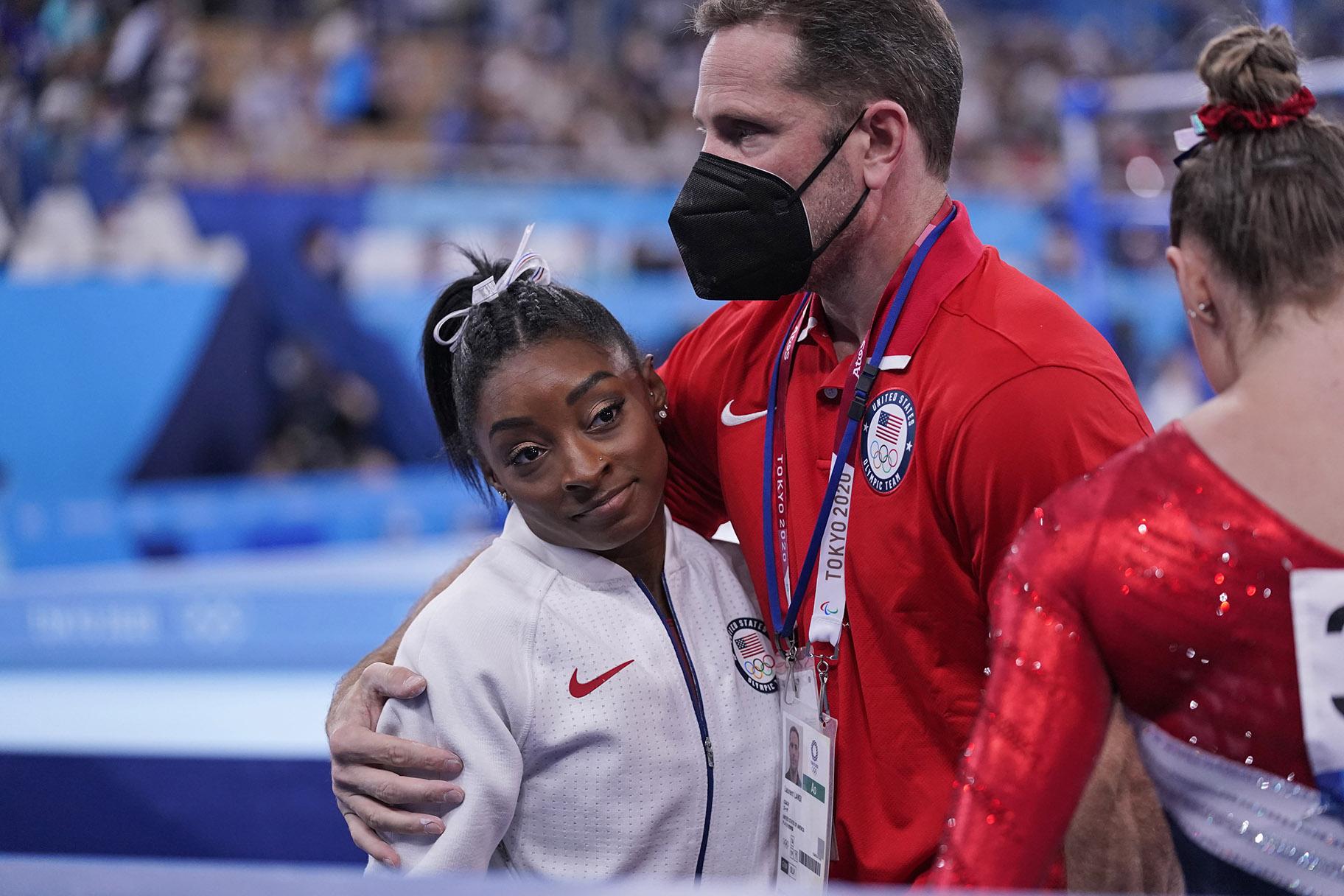 Coach Laurent Landi embraces Simone Biles, after she exited the team final with apparent injury, at the 2020 Summer Olympics, Tuesday, July 27, 2021, in Tokyo. (AP Photo / Gregory Bull)