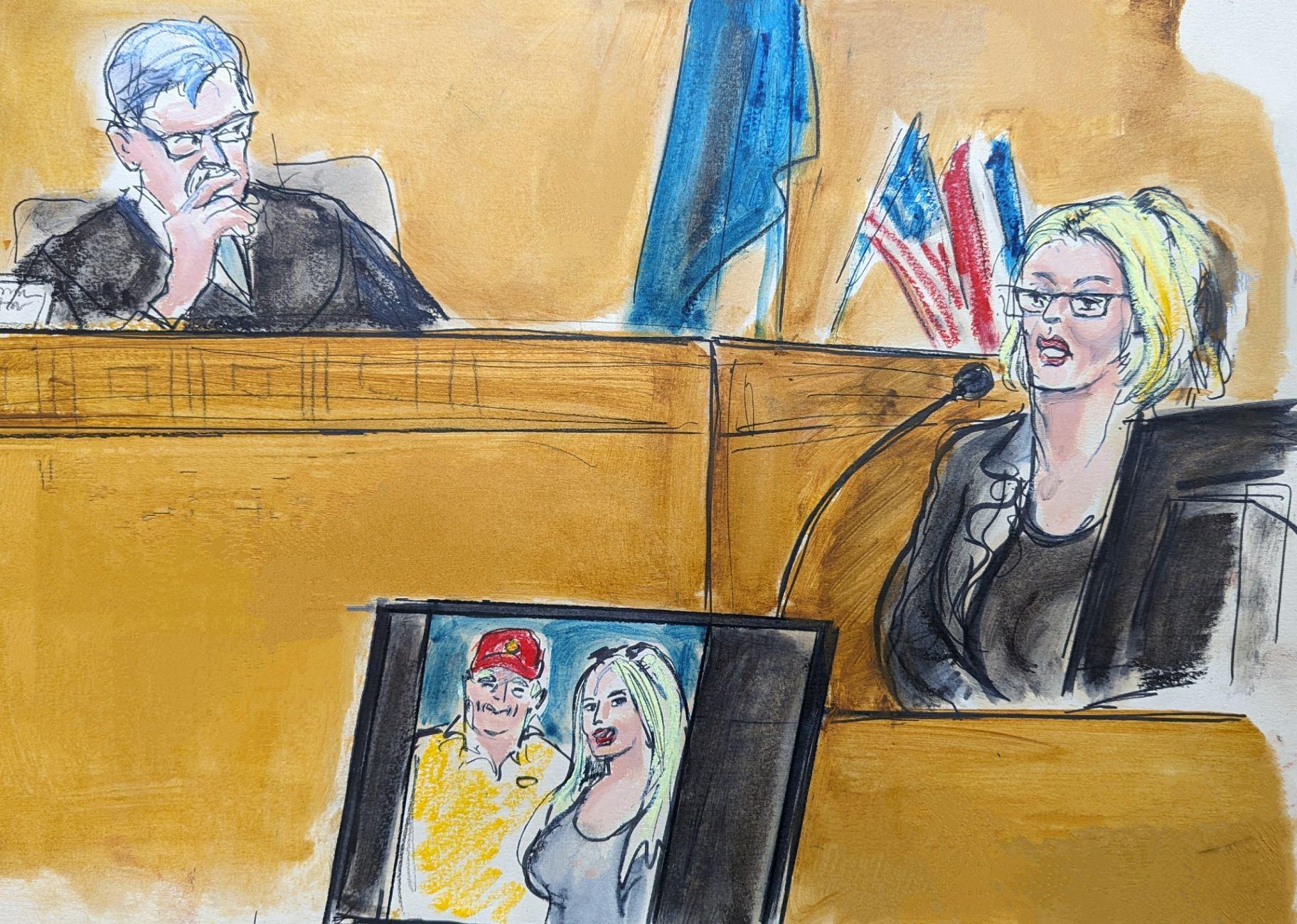 In this courtroom sketch, Stormy Daniels testifies on the witness stand as Judge Juan Merchan looks on in Manhattan criminal court, Tuesday, May 7, 2024, in New York. A photo of Donald Trump and Daniels from their first meeting is displayed on a monitor. (Elizabeth Williams via AP)